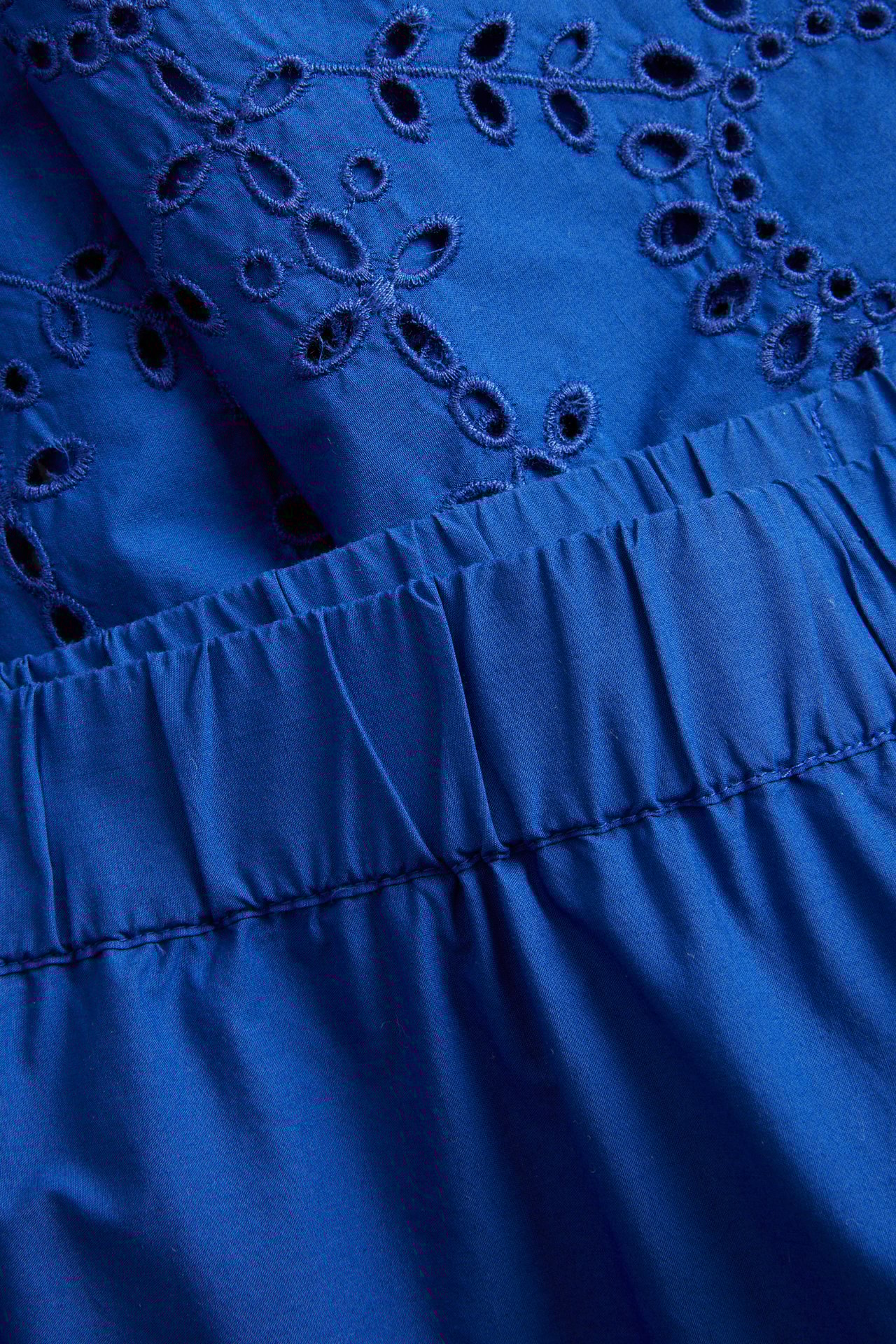 Nærbilde av blå bomullspoplin culottebukse med broderie anglaise-mønster og elastisk midje.