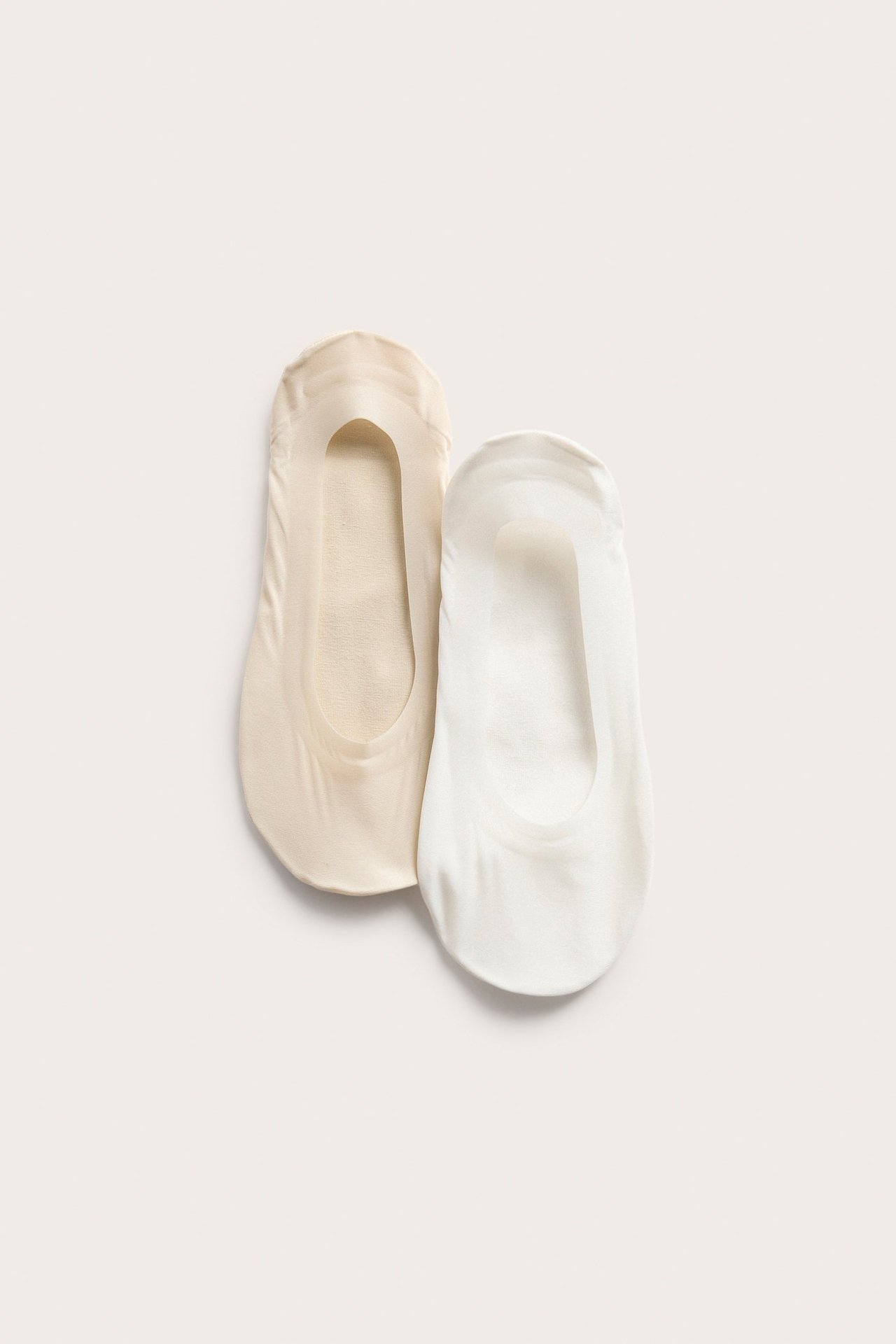 Widok z góry na dwie niewidoczne stopki: jedna kremowa, druga jasnobeżowa, z gładkiego materiału.