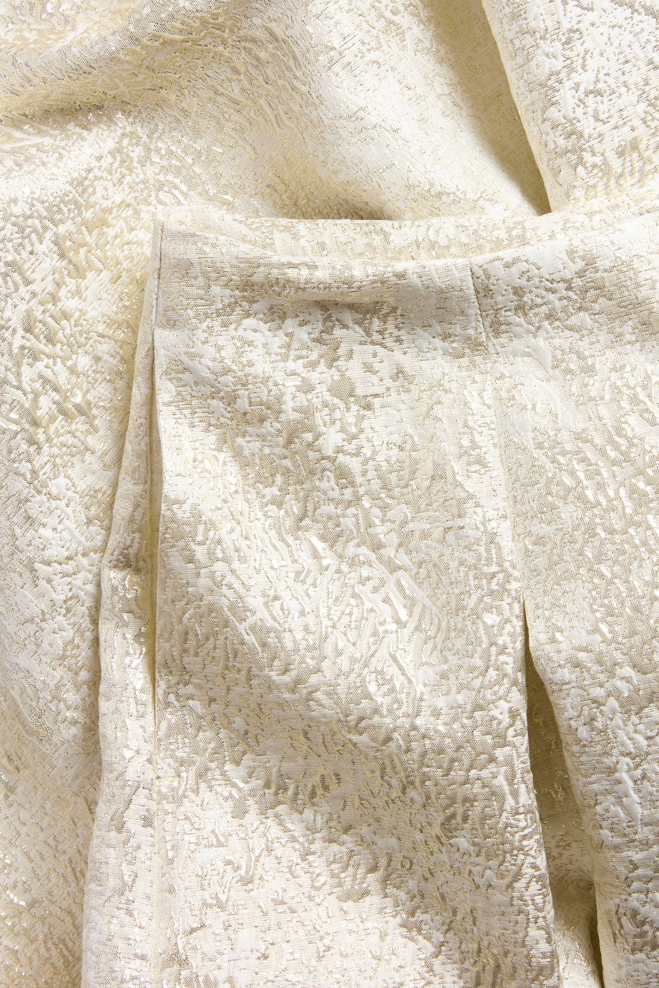 Zbliżenie na spódnicę z off-white plisowanego żakardu, ukazujące misterny tkany wzór i fakturowany materiał.