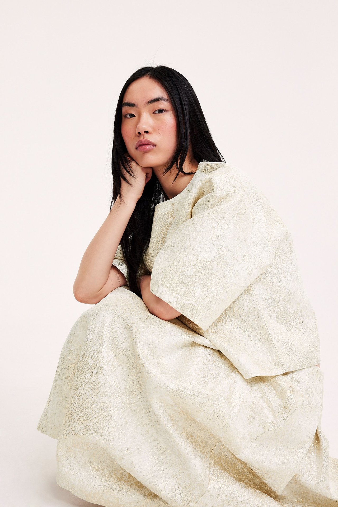 Frontvisning: Kvinne i offwhite jacquardmønstret skjørt og matchende kortermet topp, hukende.