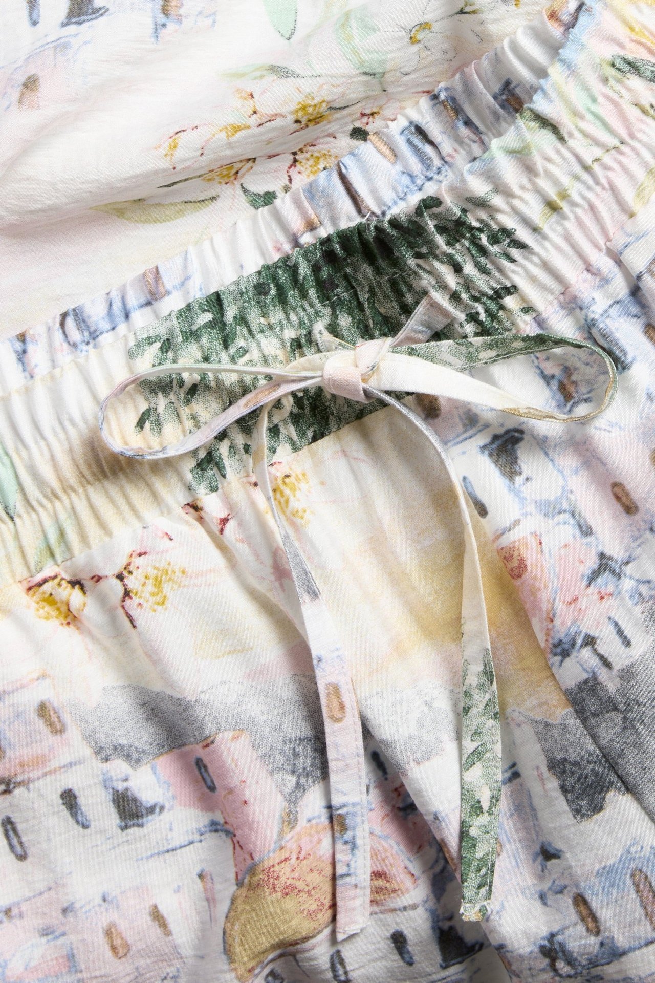 Lähikuva luonnonvalkoisista kuviollisista housuista, joissa joustava kiristysnyöri vyötäröllä, ja oliivipuita sekä sitruunoita.
