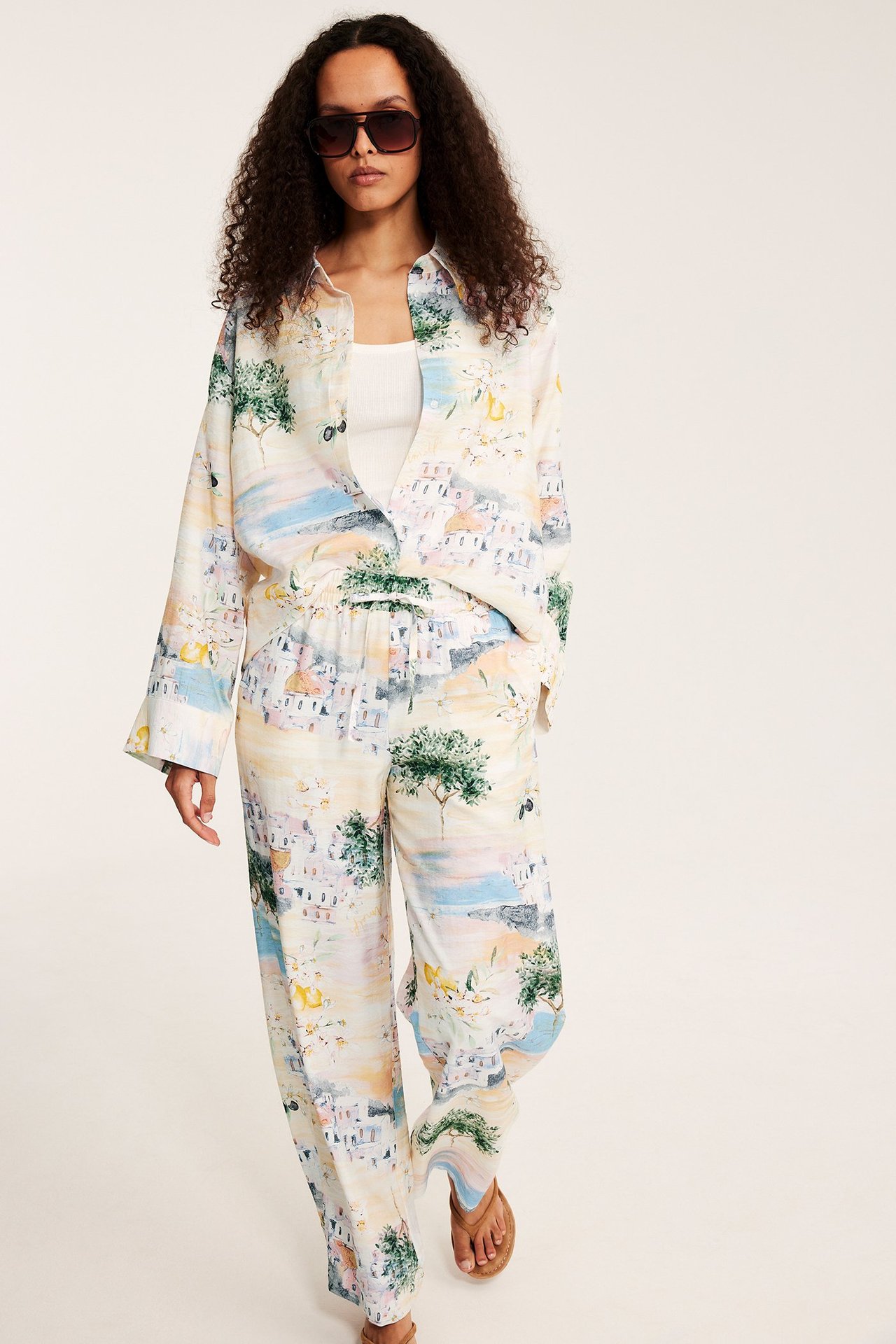 Frontvisning: Kvinne i offwhite middelhavsmønstrede vide bukser, matchende skjorte og solbriller.