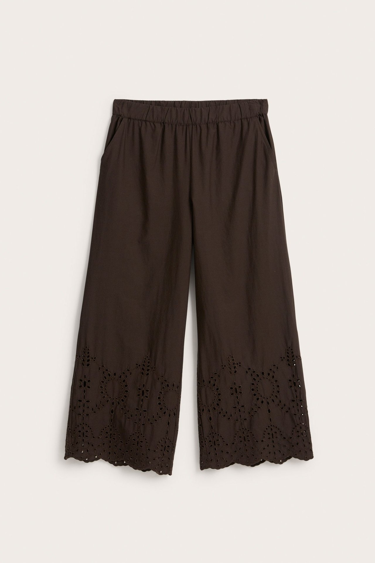 Frontbilde av mørkebrune vide bukser i bomullspoplin med strikk i midjen og broderie anglaise-kant.