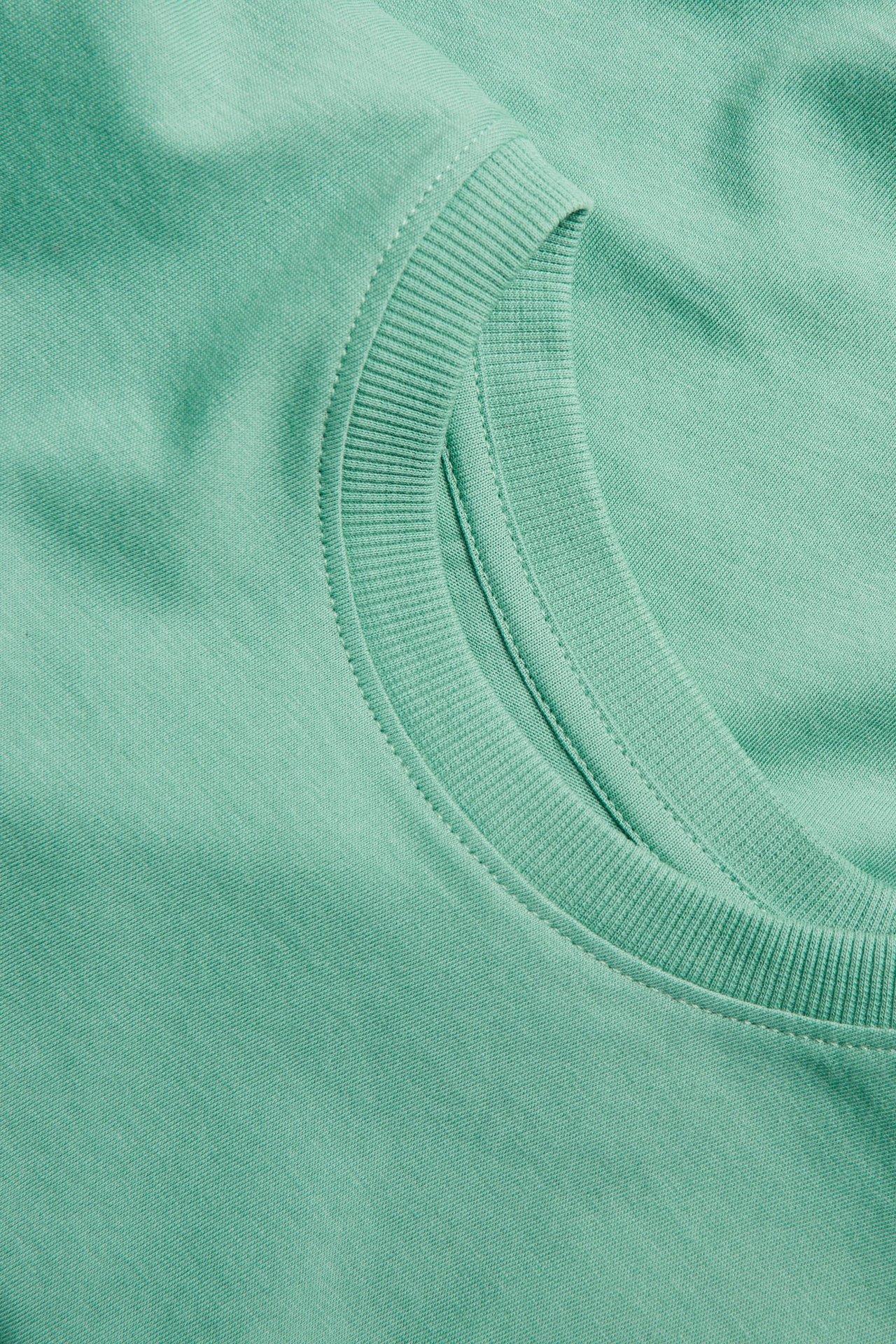 Zbliżenie na zielony jednolity bawełniany T-shirt z prążkowanym okrągłym dekoltem i widocznymi szwami.