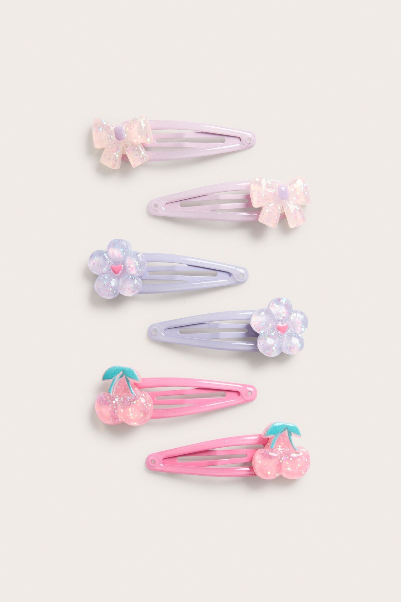 Kuusi kimaltavaa hiusklipsiä: kaksi vaaleanpunaista kirsikkaa, kaksi lilaa kukkaa, kaksi lilaa rusettia.