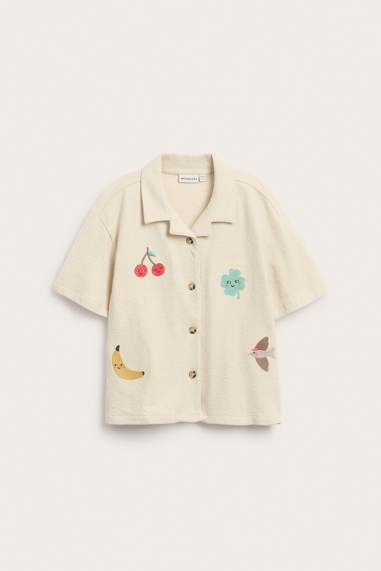 Beżowa koszula dziecięca z dzianiny, krótki rękaw, guziki z przodu, kolorowe hafty.