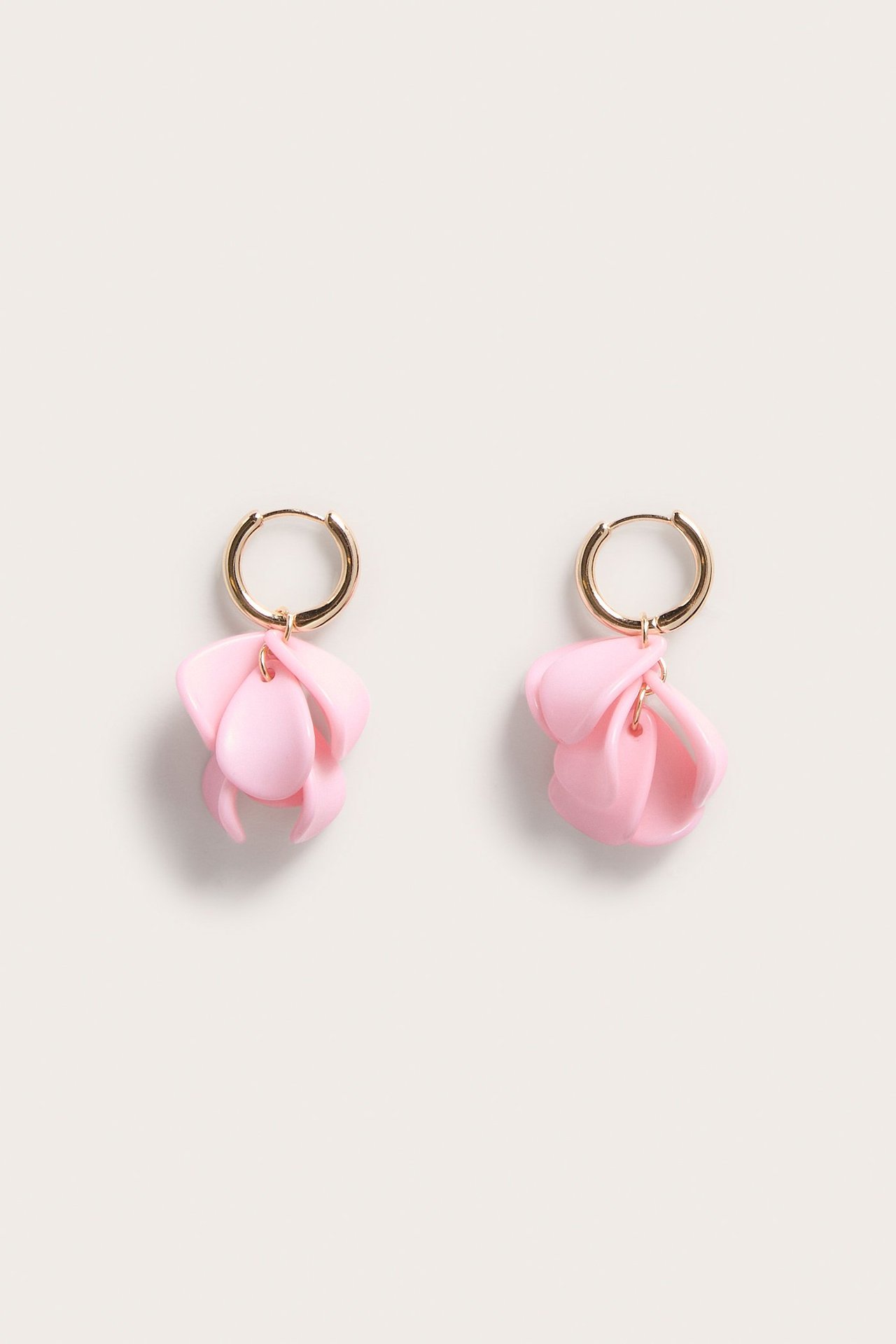 Lähikuva edestä kahdesta vaaleanpunaisesta muovikukkakorvakorusta, joissa on kullansävyiset renkaat.