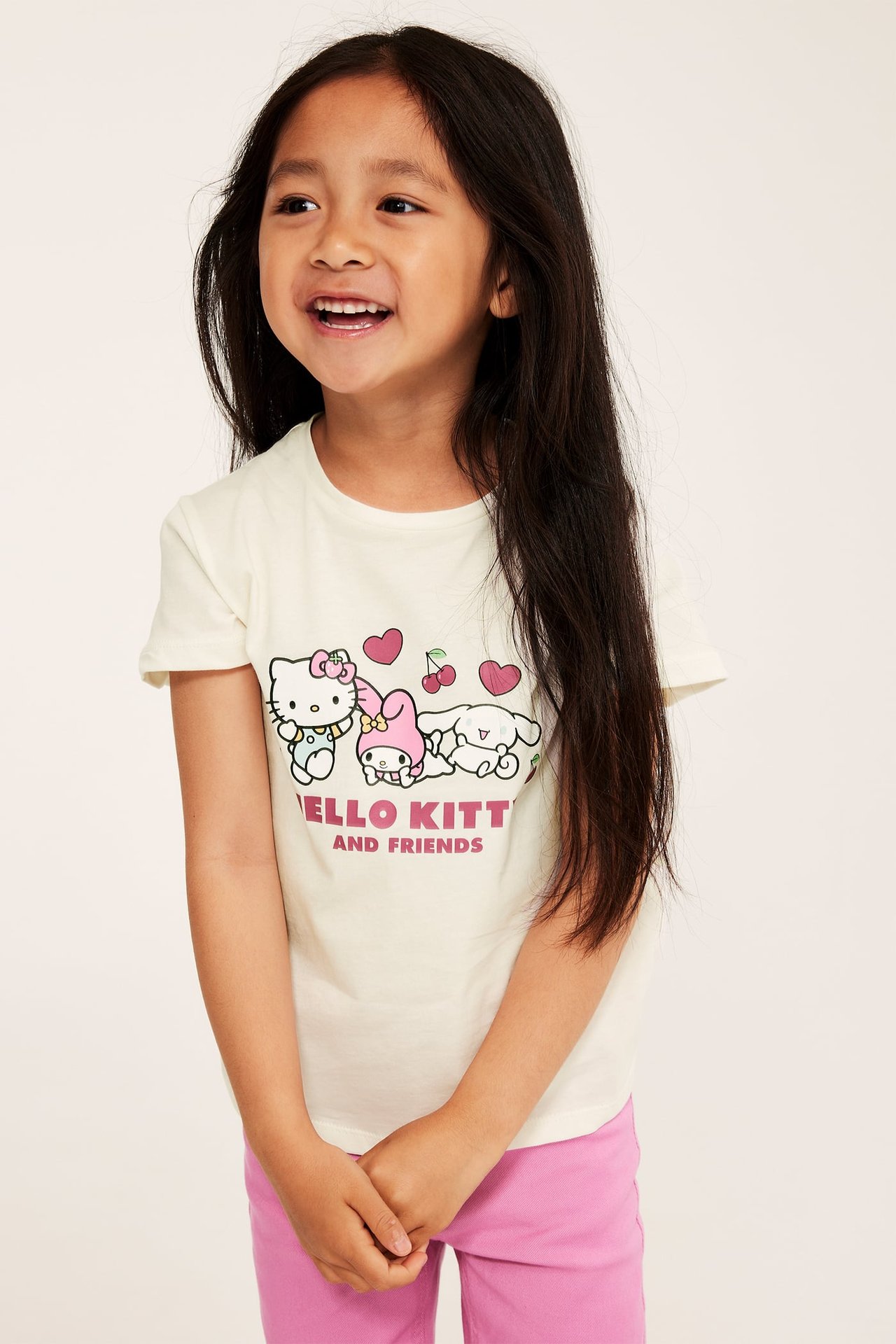 Widok z przodu: Dziecko w kremowym T-shircie z nadrukiem Hello Kitty i różowych spodniach.