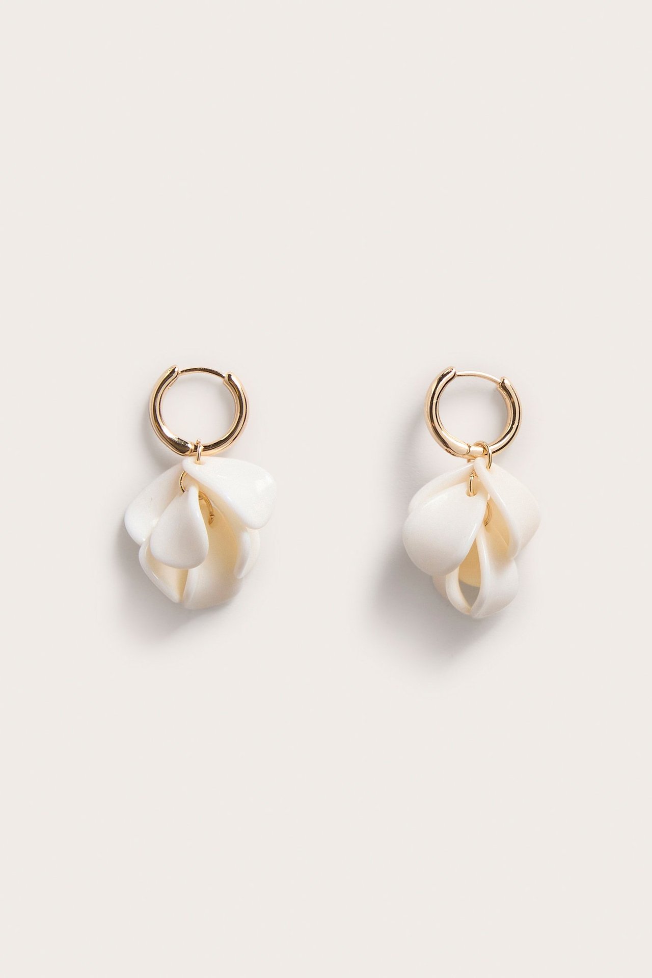 Lähikuva luonnonvalkoisista muovikukanmuotoisista korvakoruista, joissa kullanväriset rengaskiinnitykset, edestä.