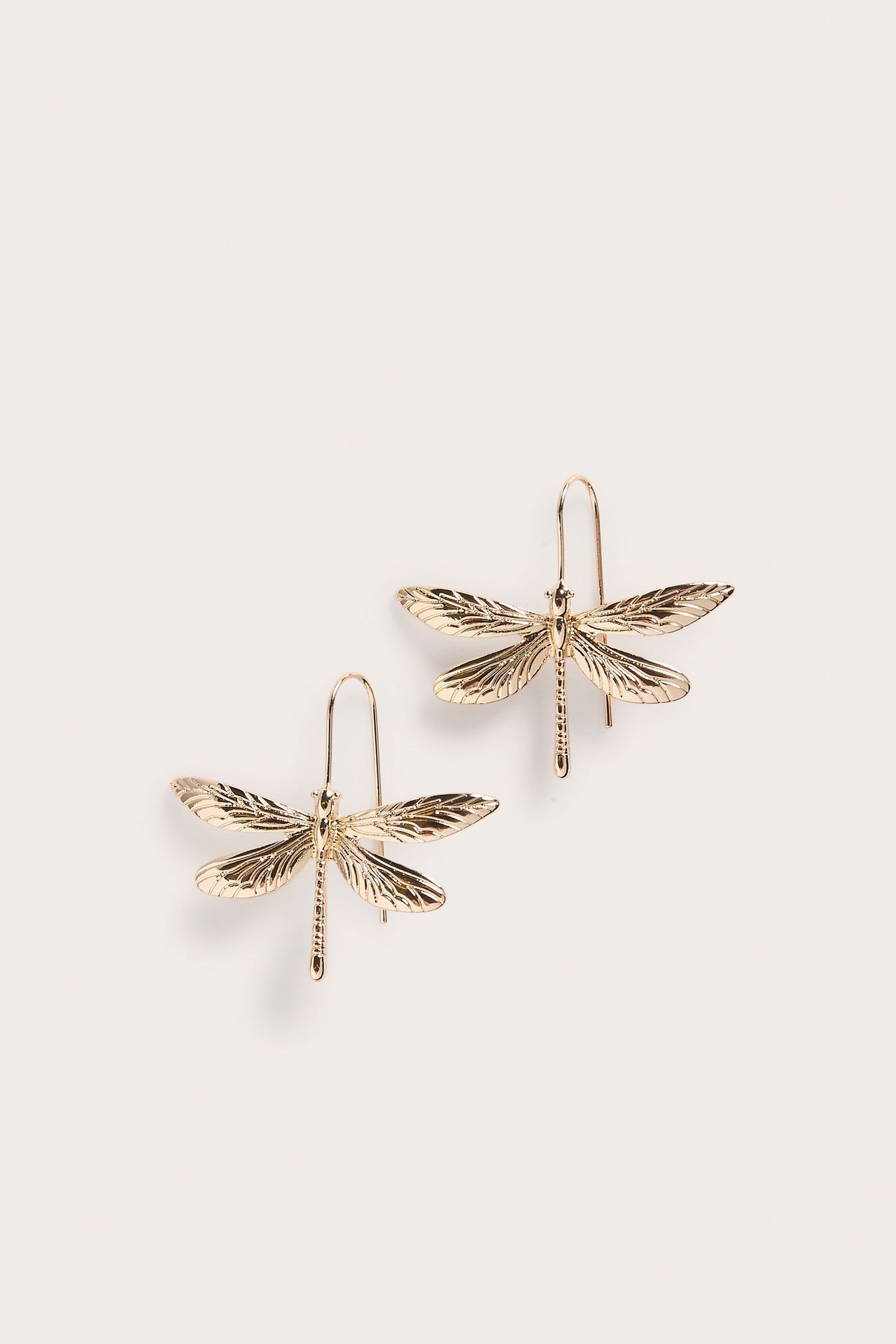 Zbliżenie dwóch złotych metalowych kolczyków ważek z zapięciem na haczyk.