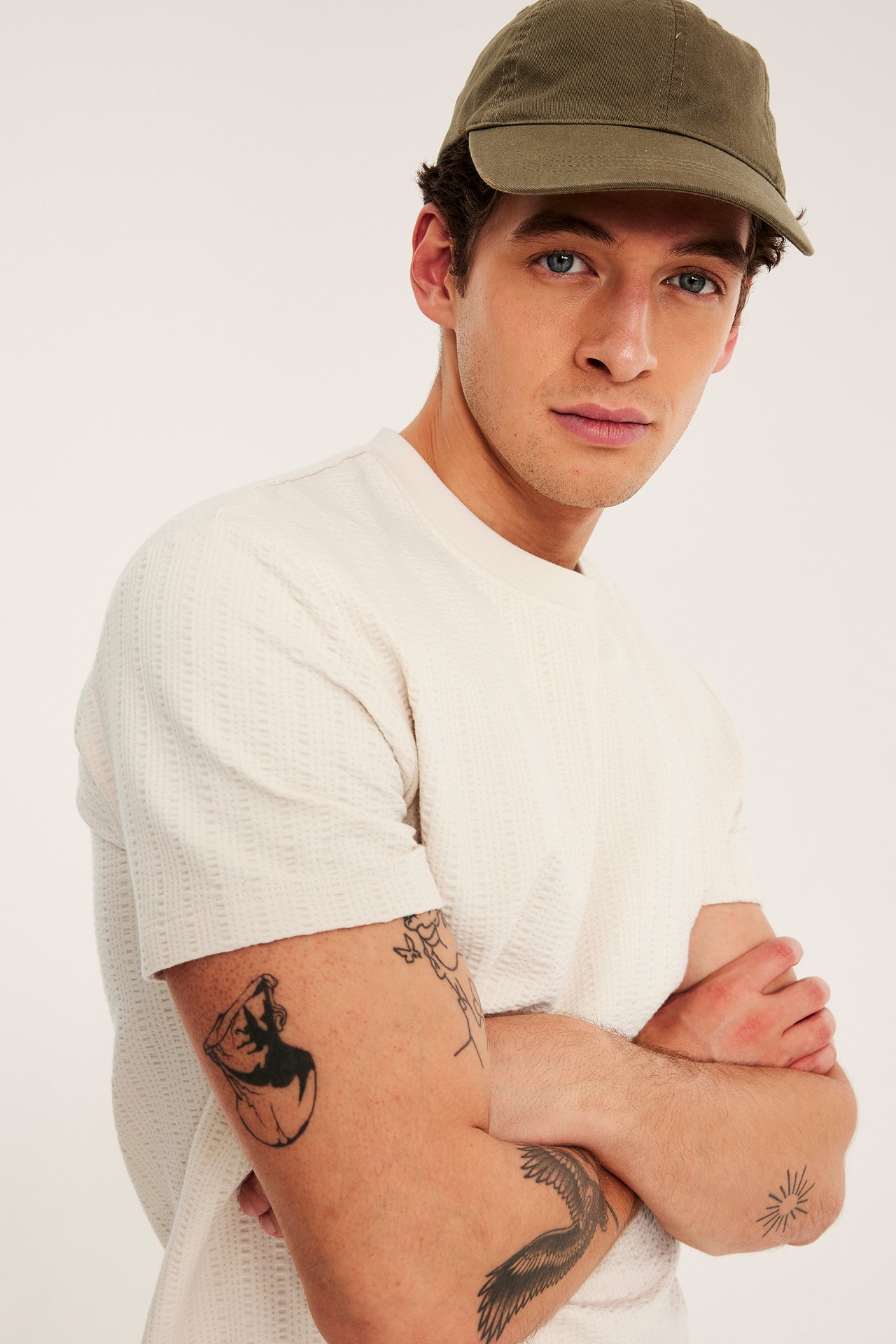 Närbild framifrån av en man i ljusbeige strukturstickad t-shirt och en olivgrön keps.