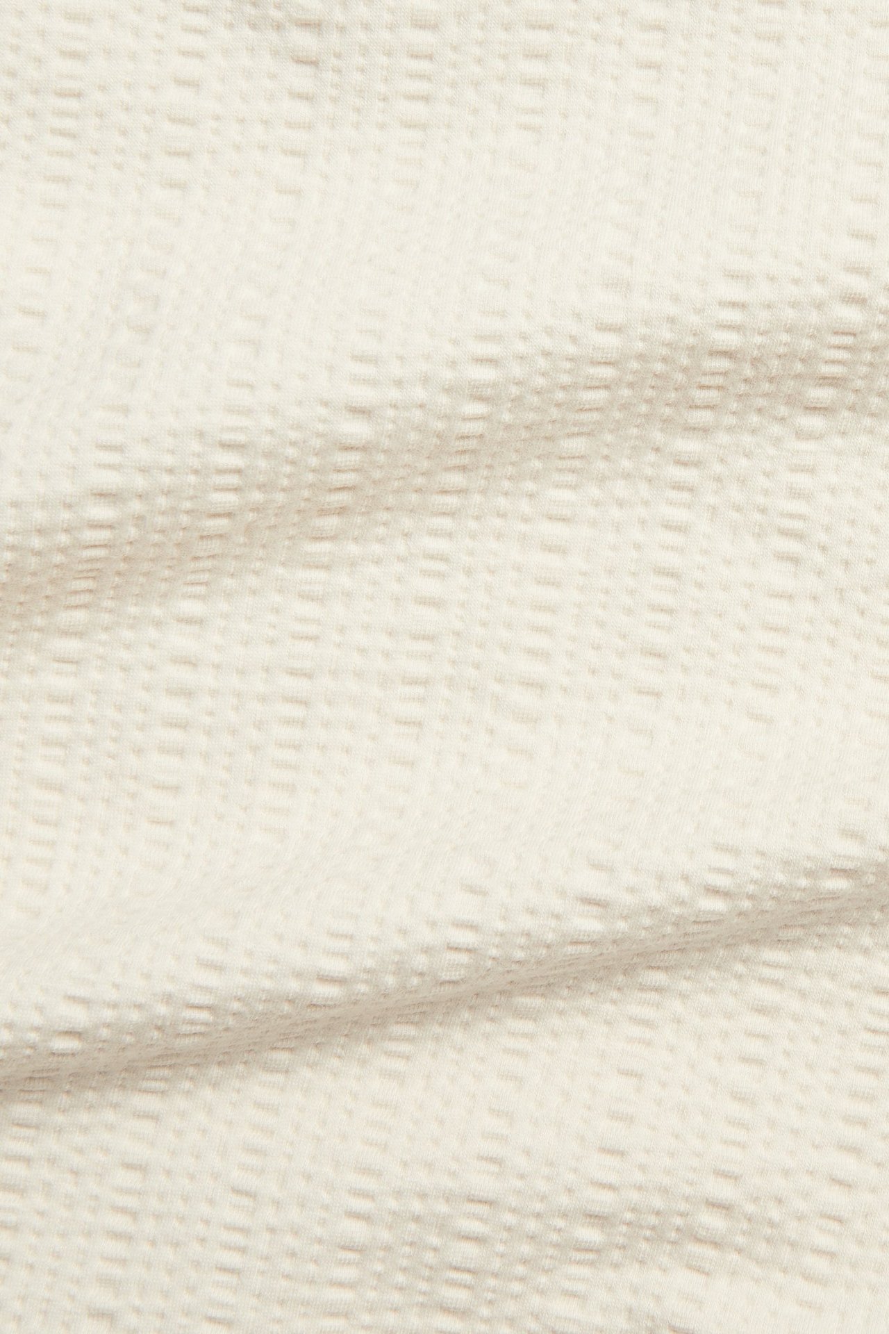 Lähikuva vaaleanbeigestä jäsennellystä puuvillasekoitteisesta t-paitakankaasta, jossa on kuvioitu rakenne.