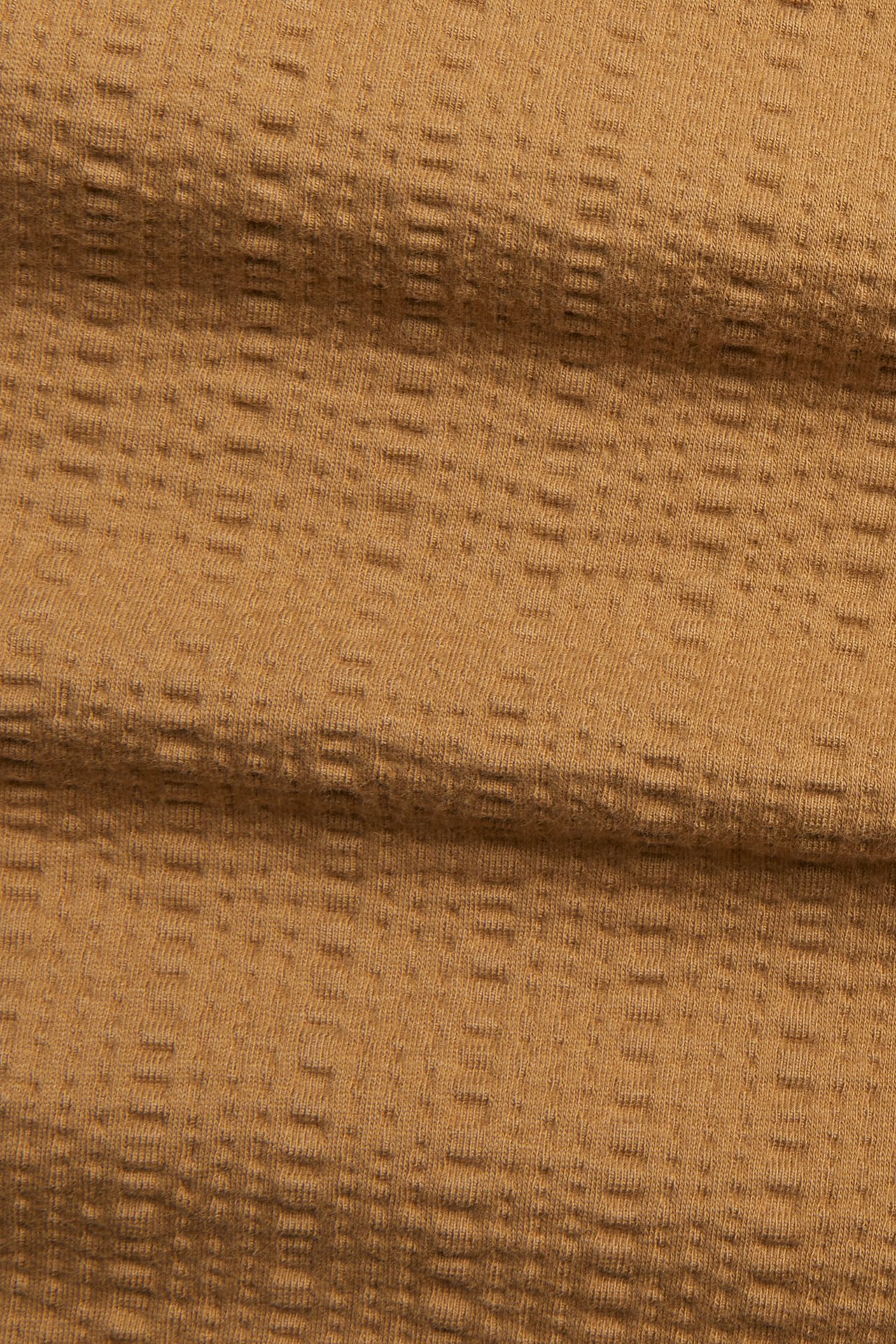 Zbliżenie na brązowy, teksturowany materiał koszulki z dzianiny.