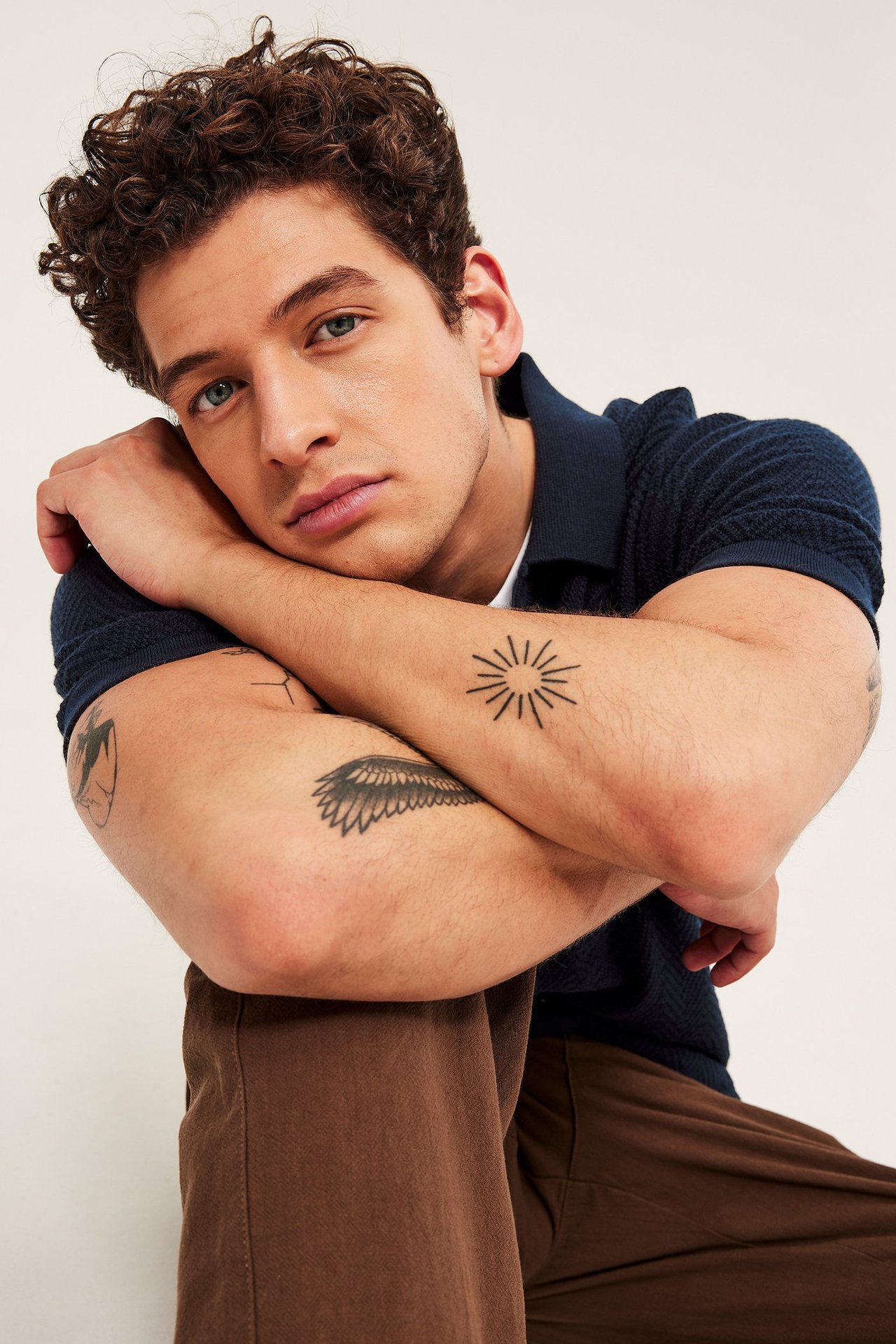 Nærbilde forfra av en mann i en mørkeblå strikket kortermet piké og brune bukser.