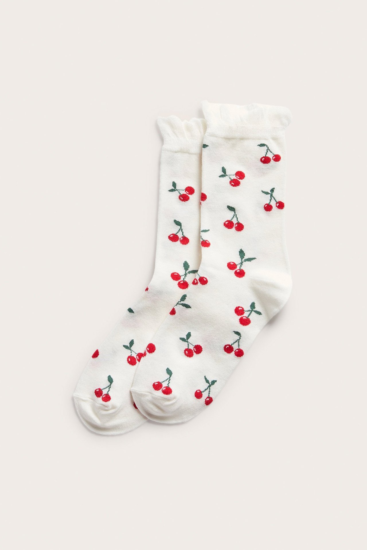 Frontbilde av hvite sokker med rødt kirsebærmønster og en volangkant øverst.