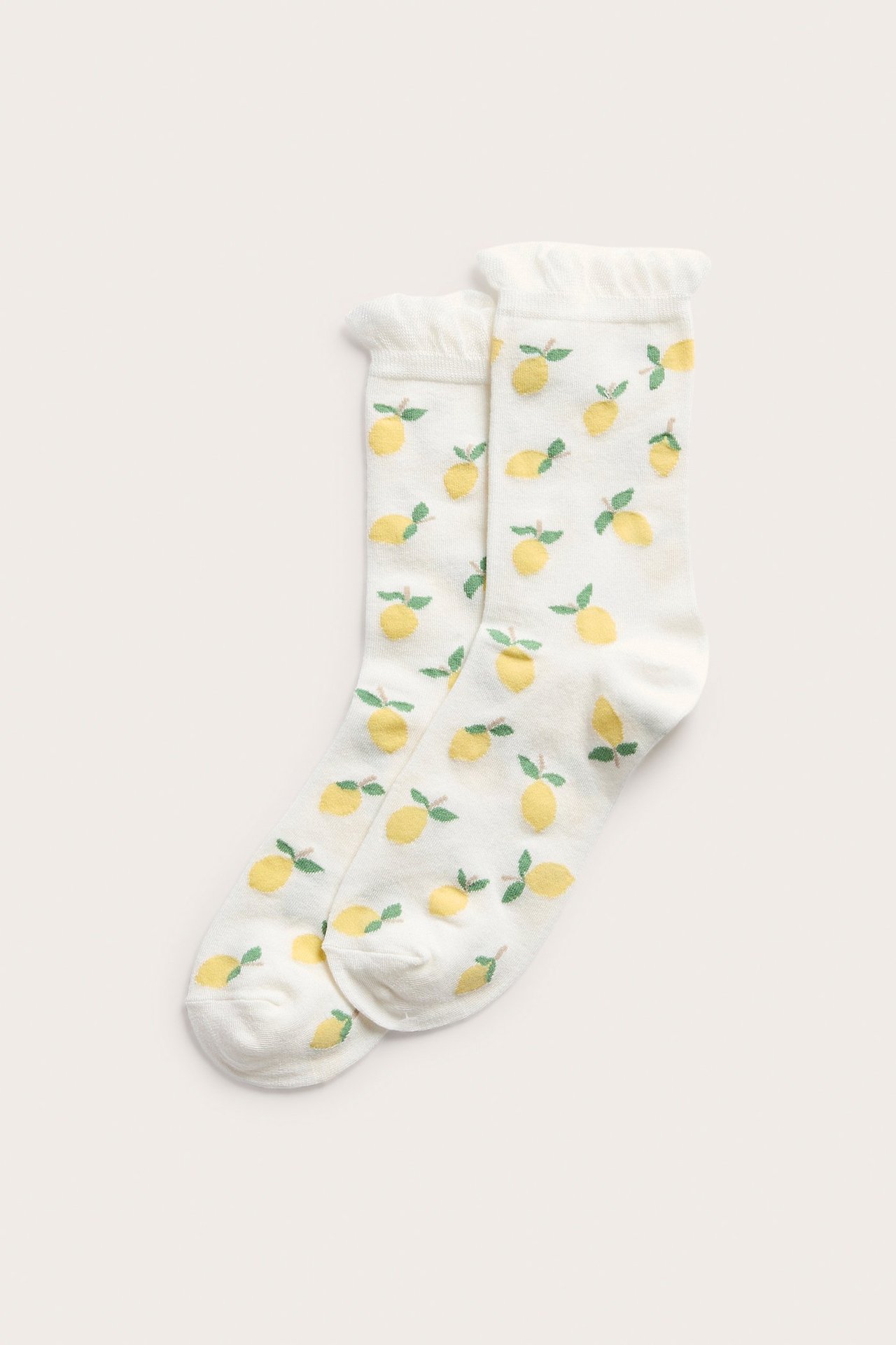 Nærbilde av to kremhvite sokker med gult sitronmønster og volangkant.