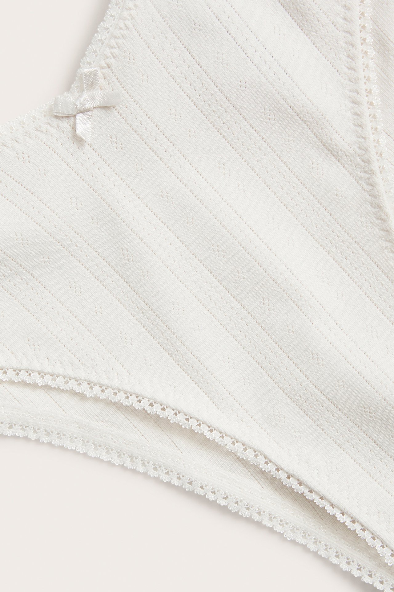 Närbild av offwhite mammabrazilian-trosa i ribbad bomull, med en liten rosett och vågig spetskant.