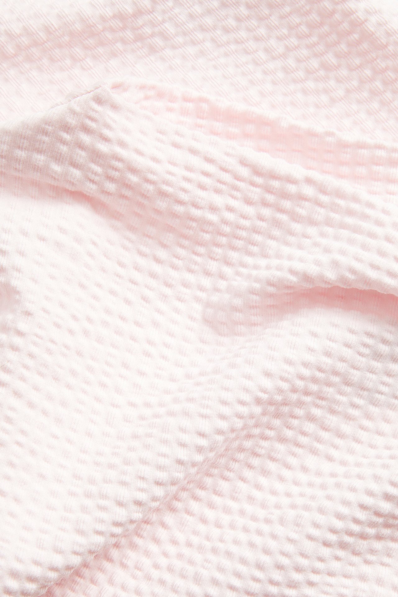 Närbild av ljusrosa bäckebölja-topptyg med ett subtilt texturerat mönster.