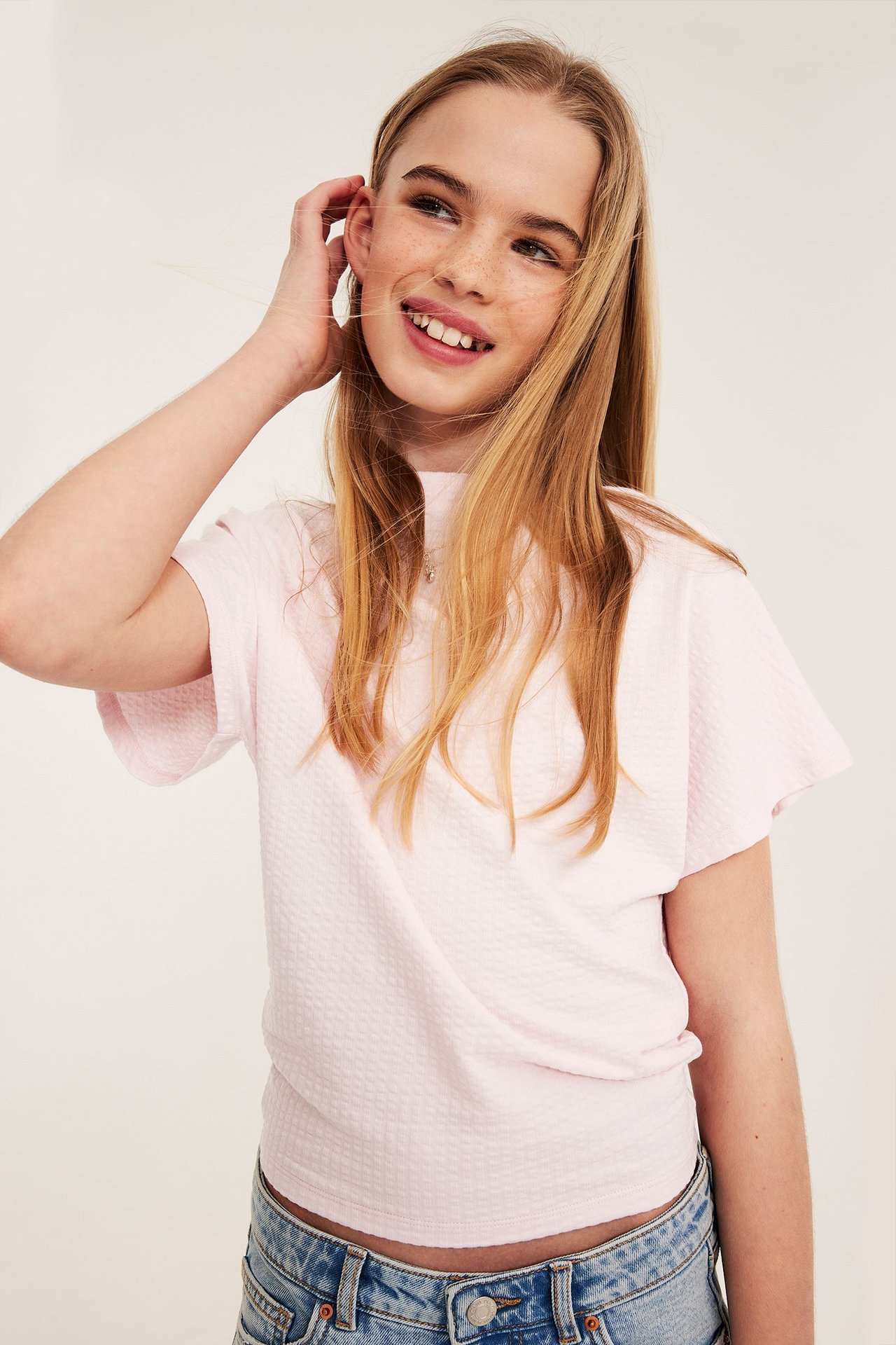 Edestä: Tyttö yllään vaaleanpunainen kuvioitu pystykaulus toppi leveillä hihoilla ja farkut.