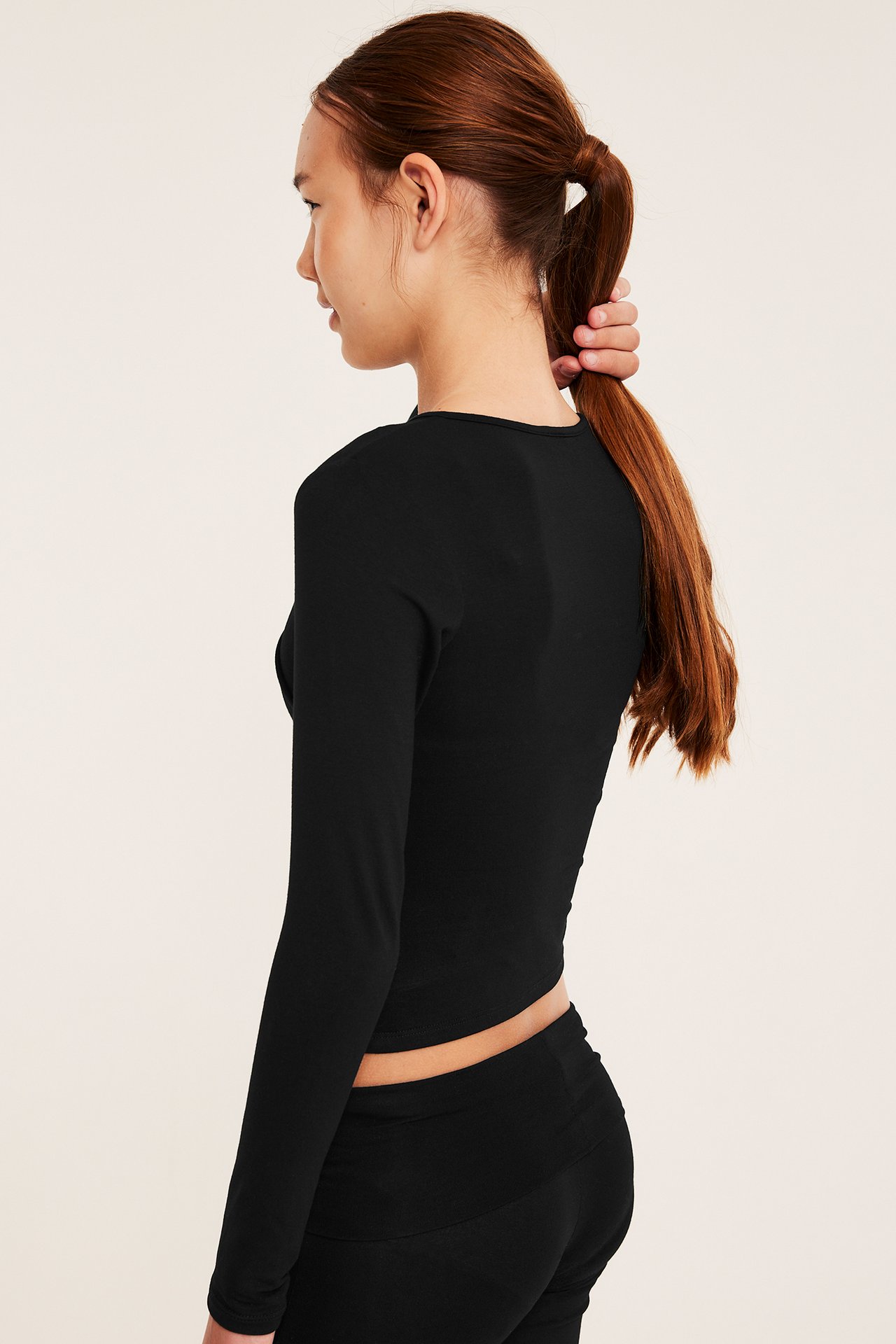 Sidovy av kvinnlig modell med svart långärmad croptop och svarta åtsittande byxor.