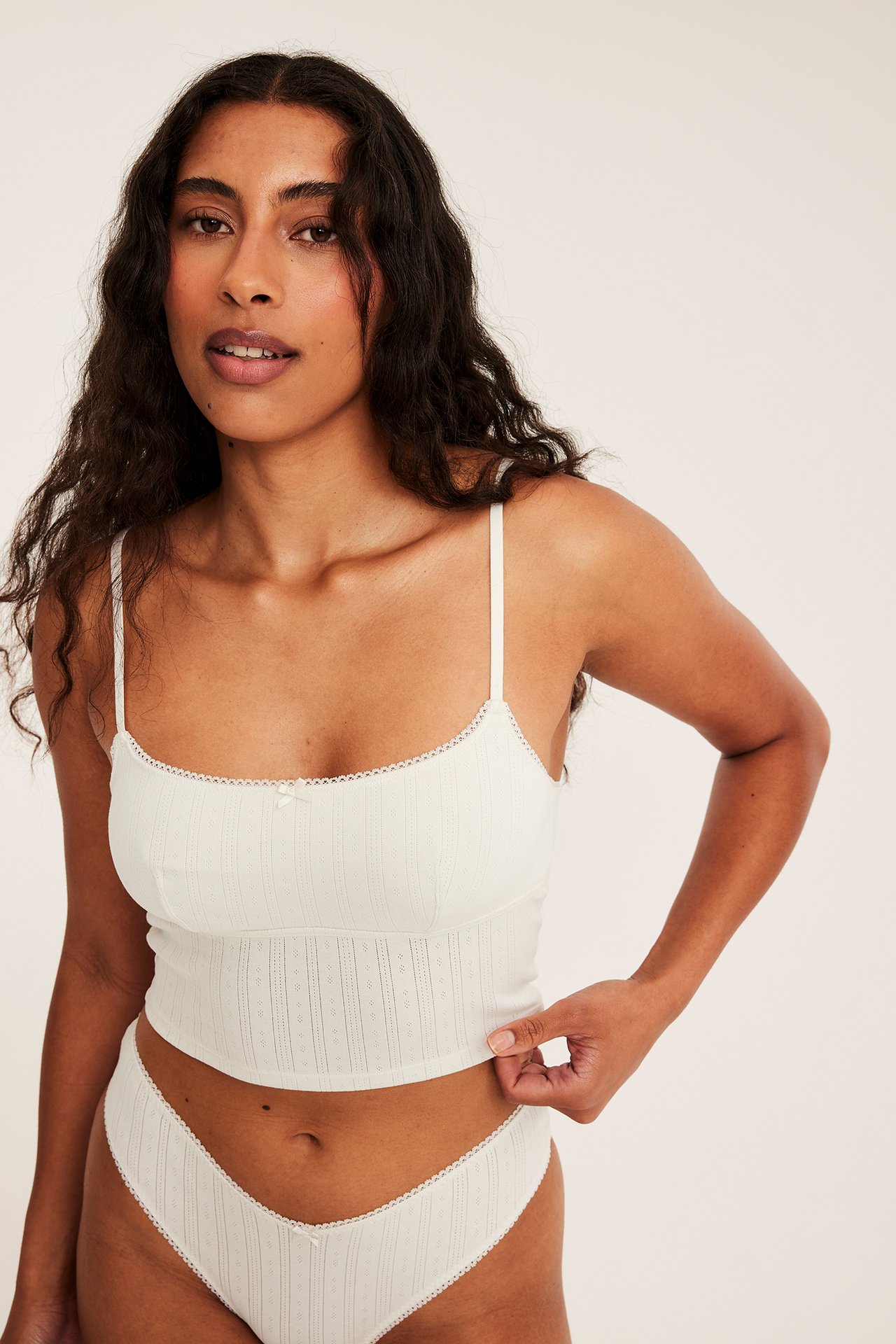 Framifrån, kvinna i offwhite pointelle bralette topp med justerbara band och matchande trosa.