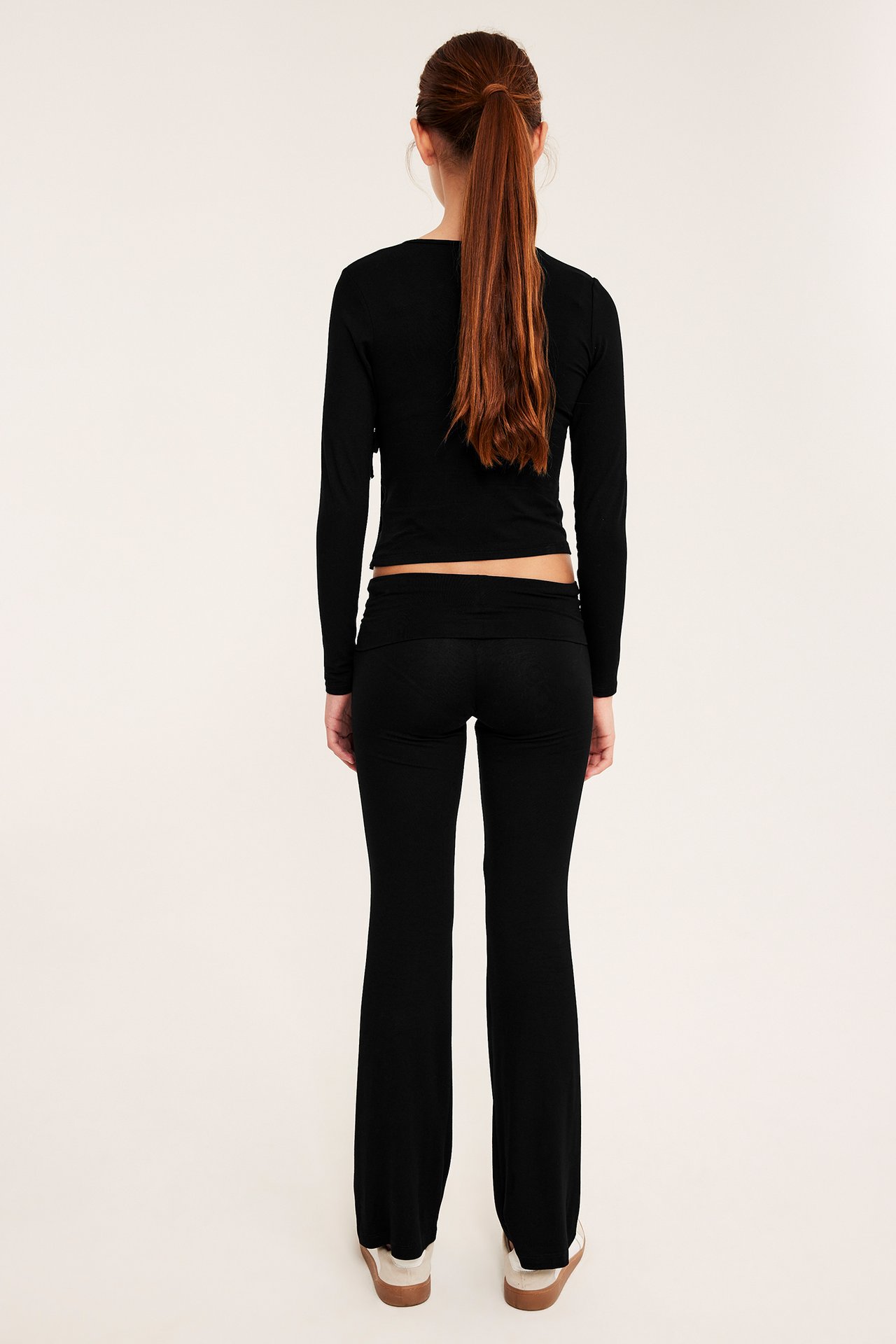 Kvinne sett bakfra: svart langermet croptop, svarte yogabukser, beige joggesko.