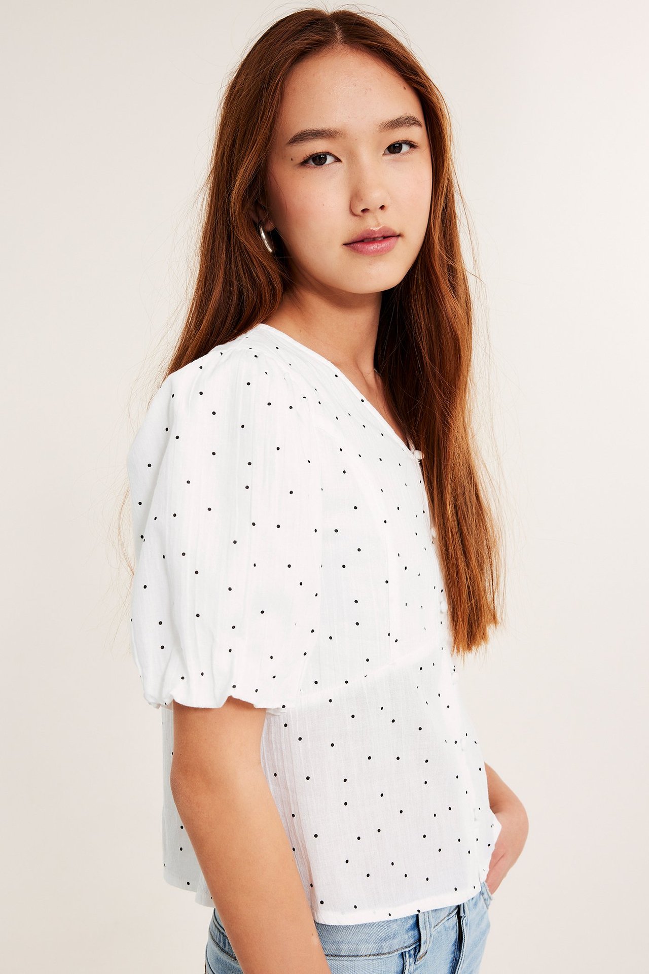 Forfra: Barn iført hvit prikkete bluse med puffermer og tildekkede knapper, og lyse jeans.