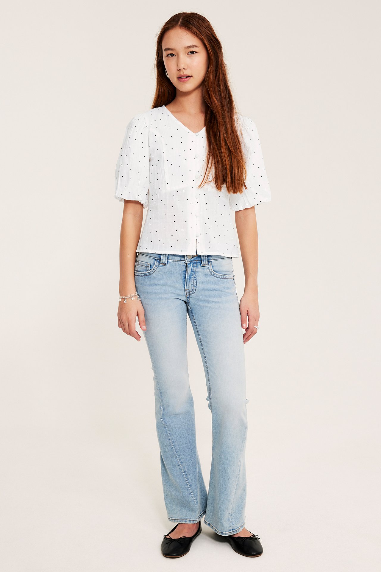 Forfra: barn i hvit prikkete bluse med puffermer, lyseblå utsvungne jeans og svarte ballerinasko.