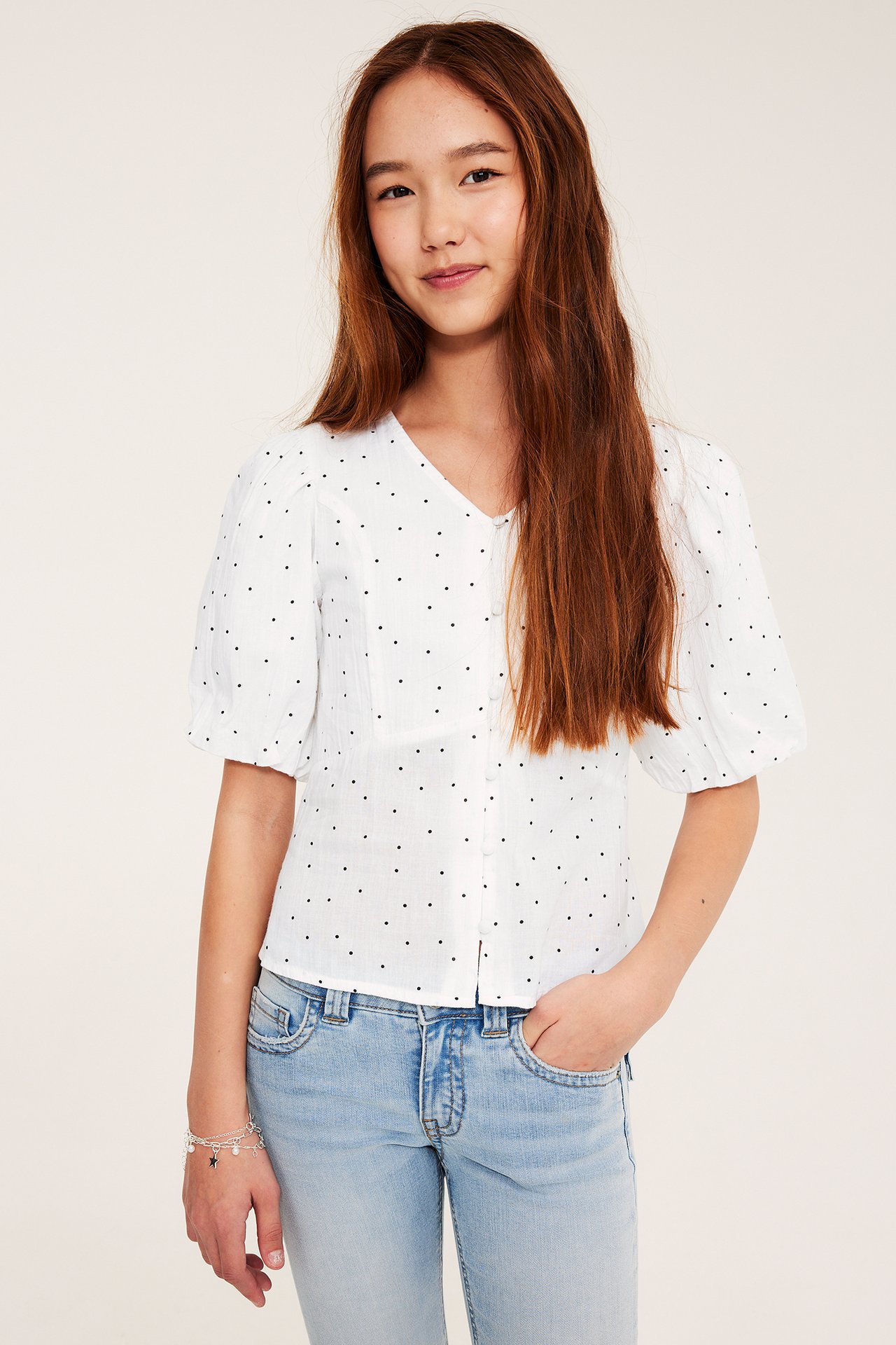 Frontbilde av et barn iført hvit prikkete bluse med puffermer og lyseblå jeans.