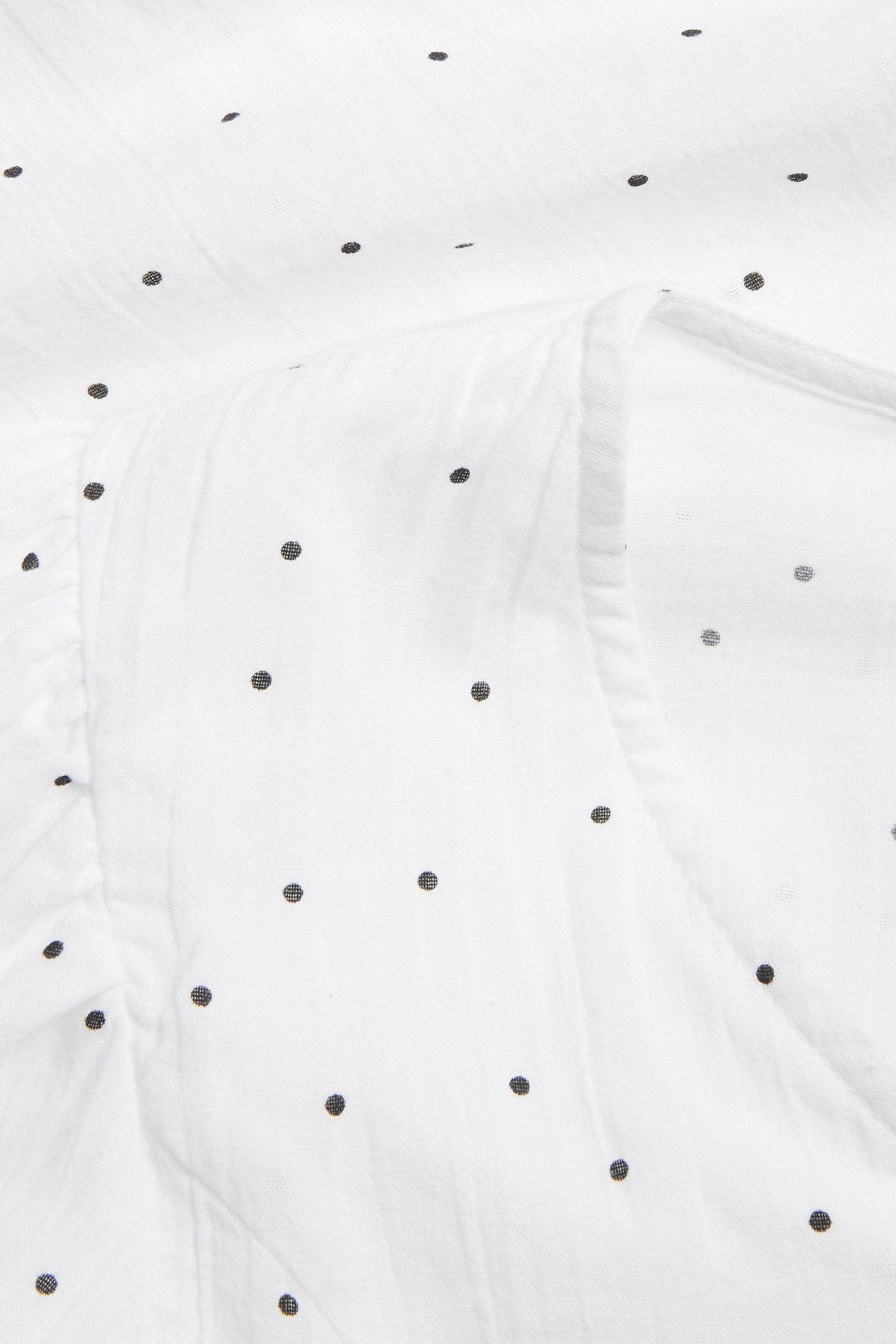 Närbild av vitt bomullsblustyg med små svarta prickar och lätt rynkning.
