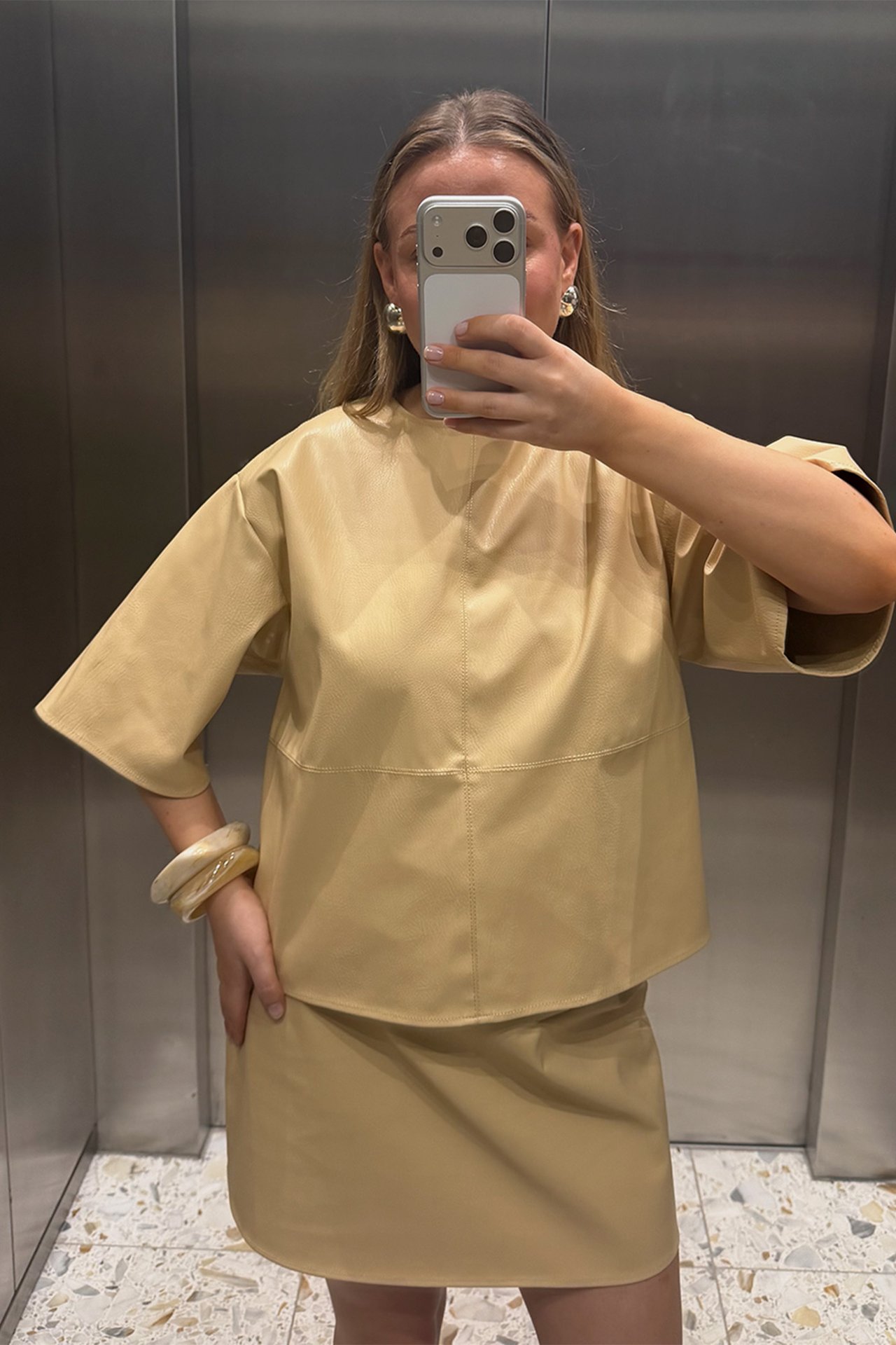 Widok z przodu: kobieta w jasnożółtym T-shircie ze sztucznej skóry, pasującej spódnicy, kolczykach i bransoletkach.