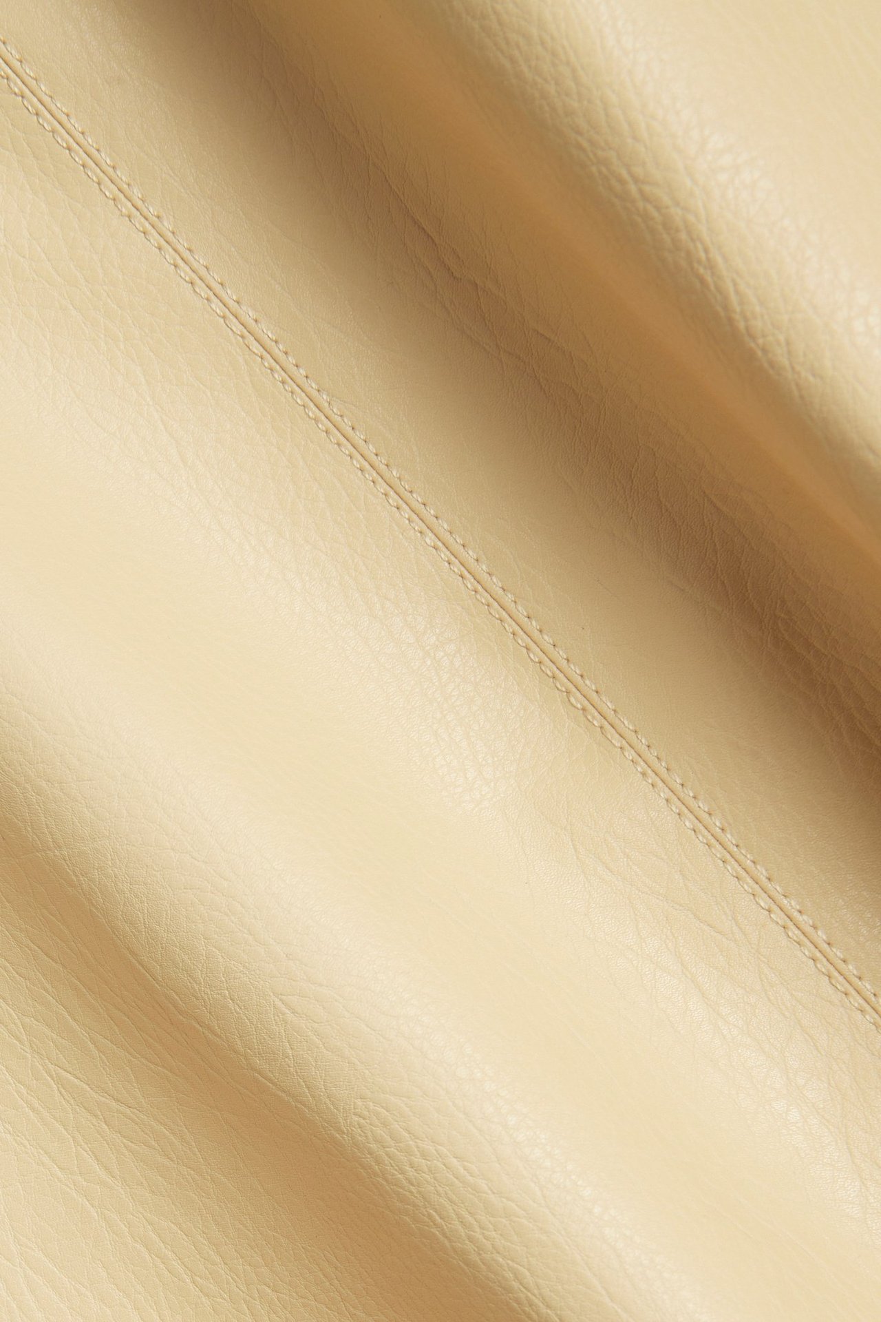 Lähikuva vaaleankeltaisesta keinonahkakankaasta topissa, näkyvin ompelein.