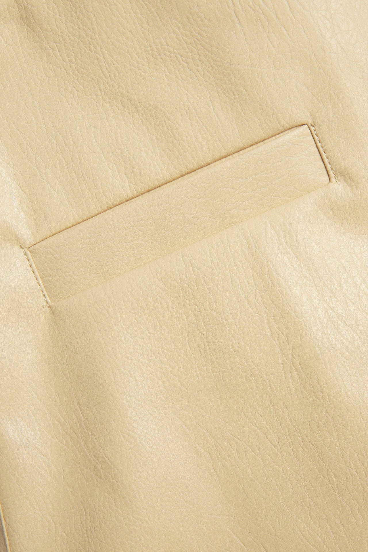 Lähikuva vaaleankeltaisesta tekonahkaisesta lyhyestä hameesta, jossa on vaakasuora läppätasku.