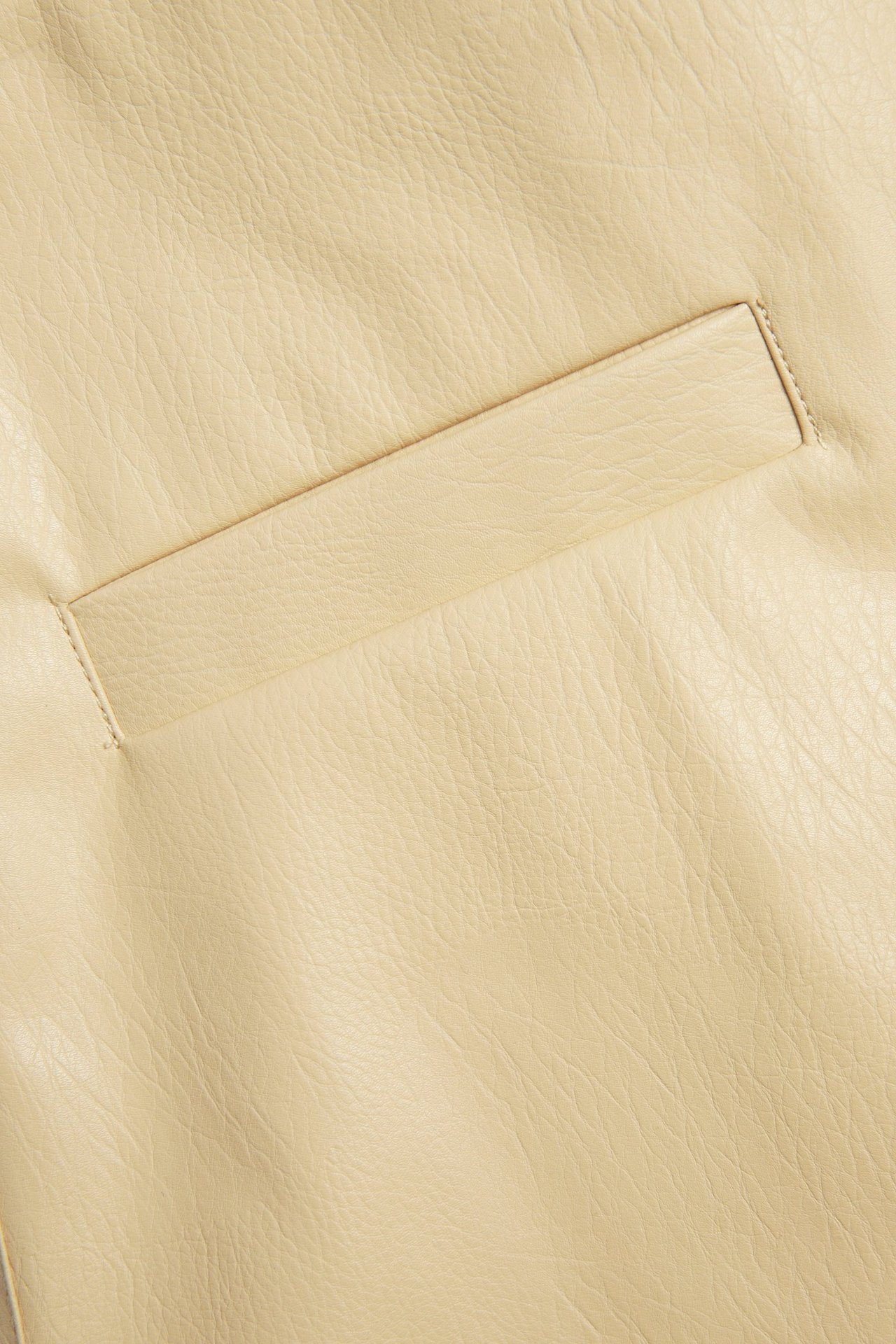 Zbliżenie na jasnożółtą krótką spódnicę ze sztucznej skóry, z poziomą kieszenią z wypustką.