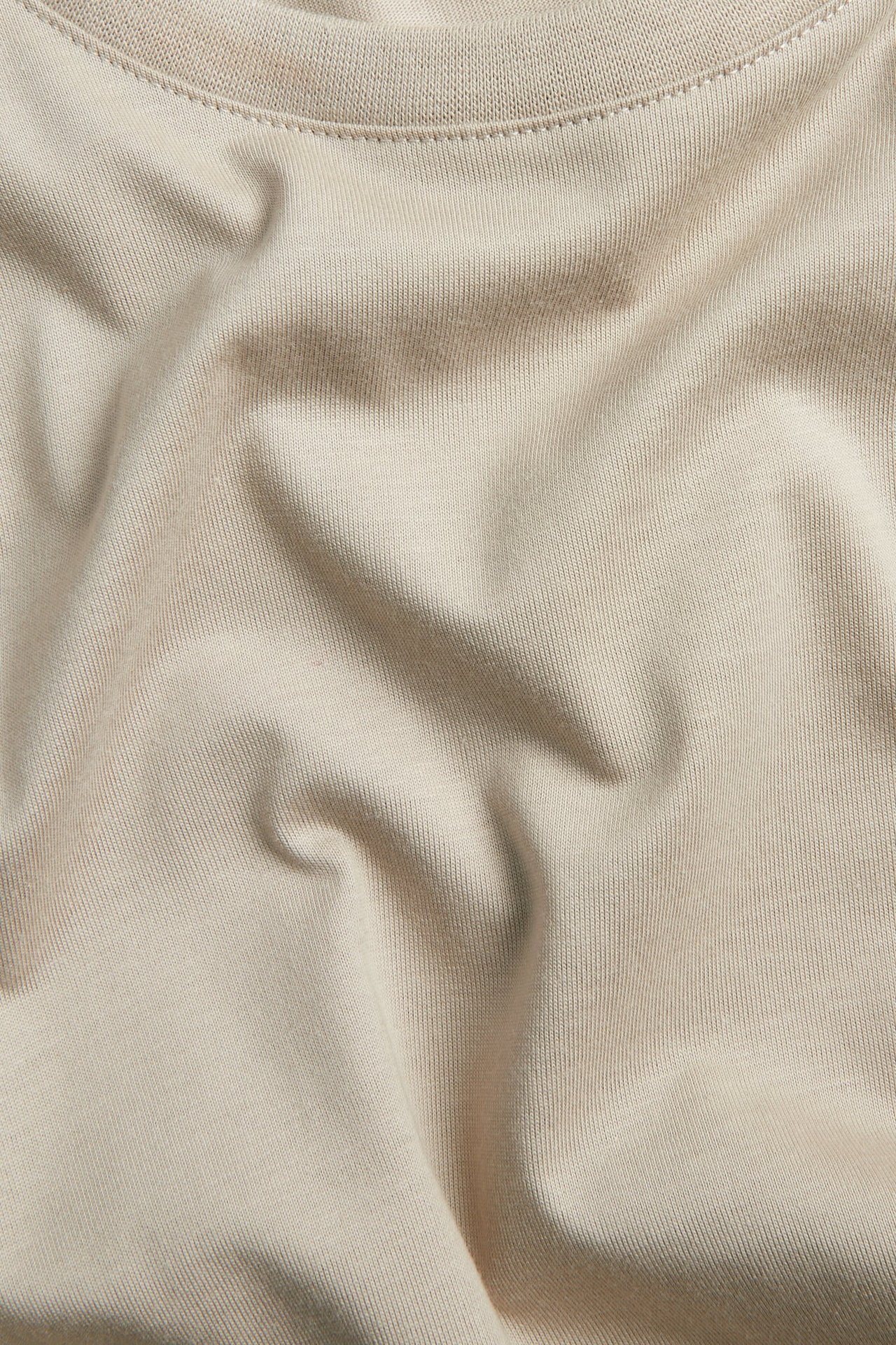 Närbild på en skrynklig ljusbeige jerseyt-shirt.