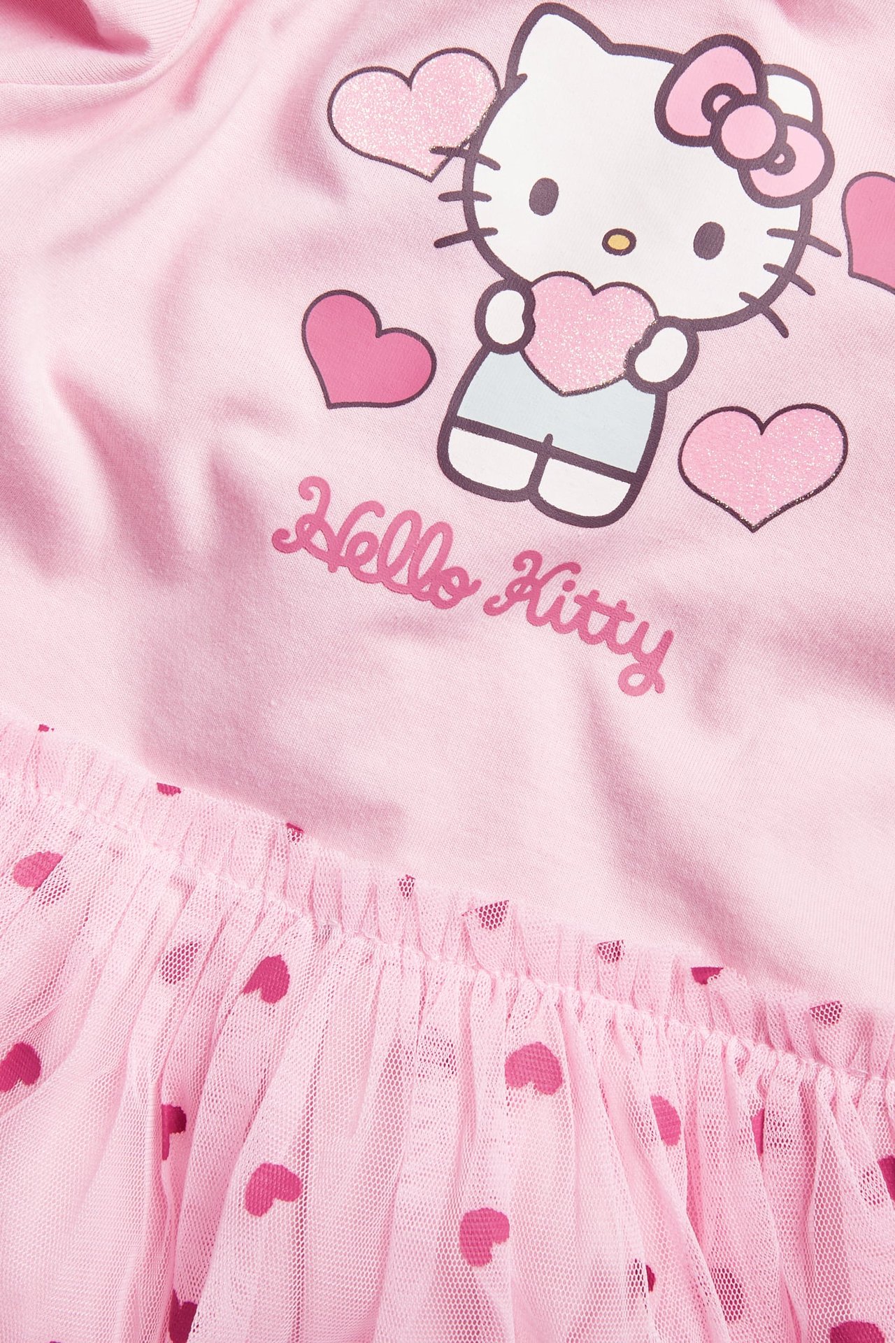 Zbliżenie różowej sukienki dziecięcej z nadrukiem Hello Kitty w serca i falbankową tiulową spódnicą w serca.