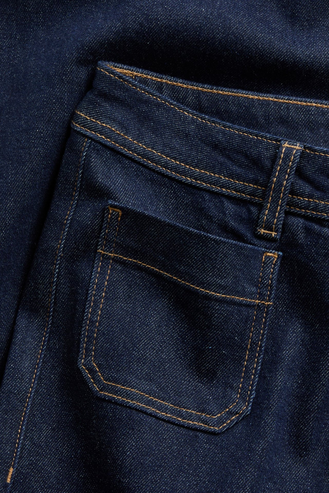 Zbliżenie ciemnoniebieskich jeansów z denimu z jasnobrązowymi szwami i detalami przedniej kieszeni.