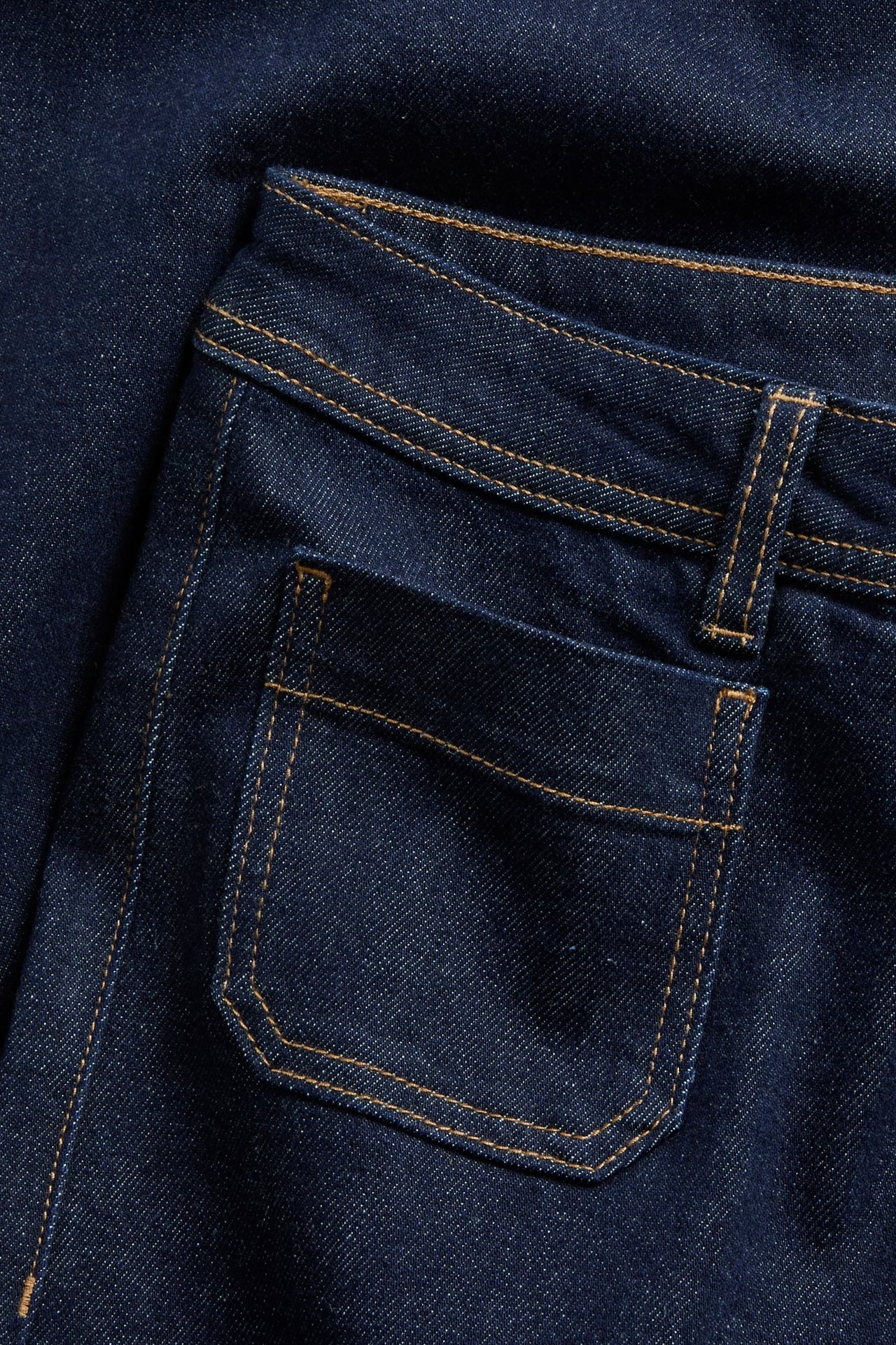Zbliżenie ciemnoniebieskich jeansów z denimu z jasnobrązowymi szwami i detalami przedniej kieszeni.