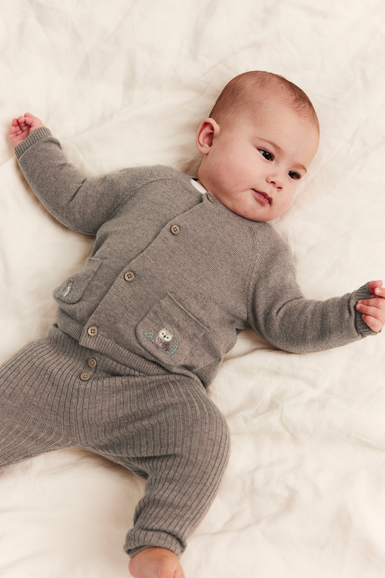 Baby i grå strikket cardigan med uglebroderi og matchende ribbete bukser, forfra.