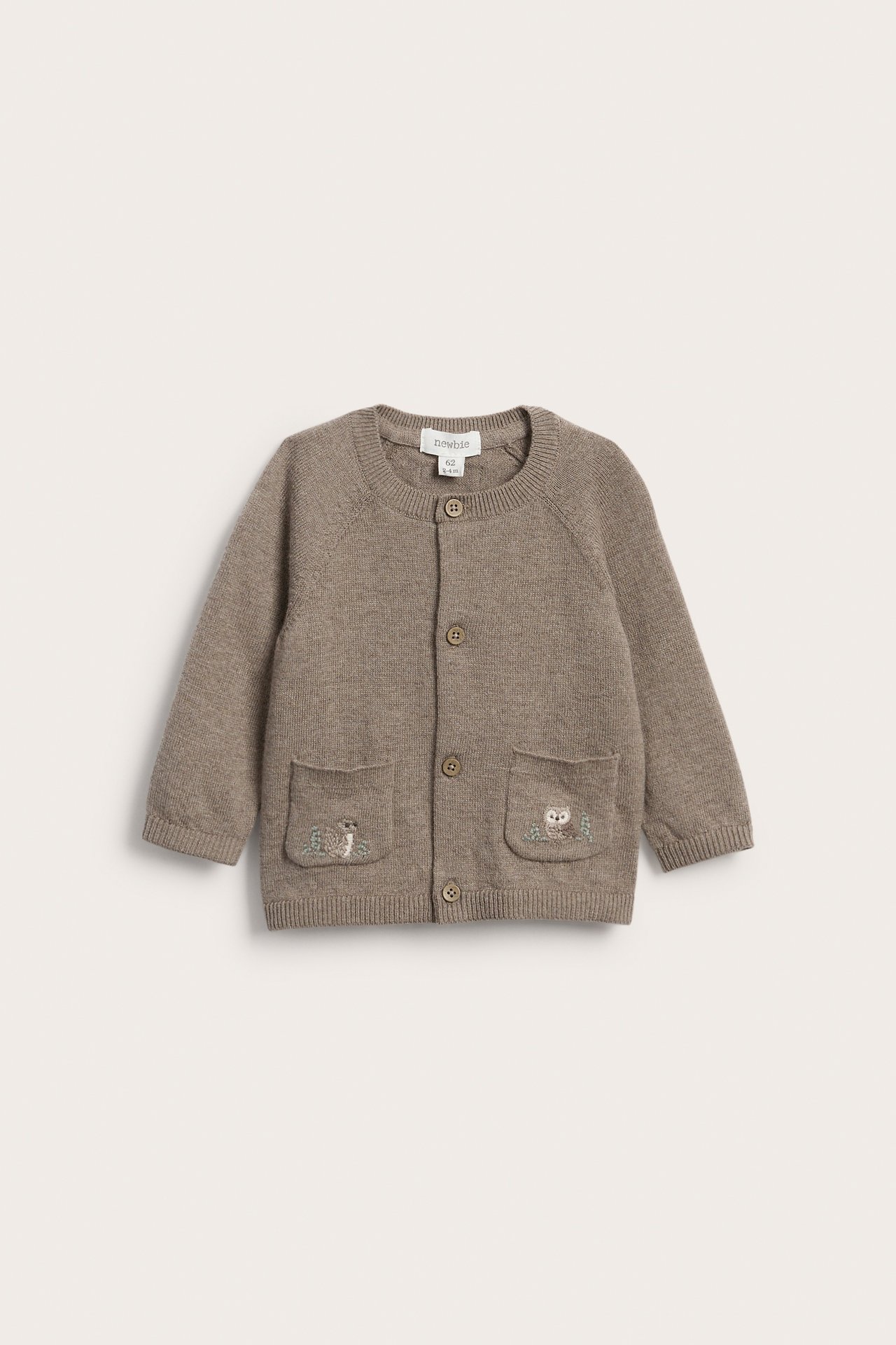 Frontbilde av brun strikket babyjakke med knapper og broderte lommer.