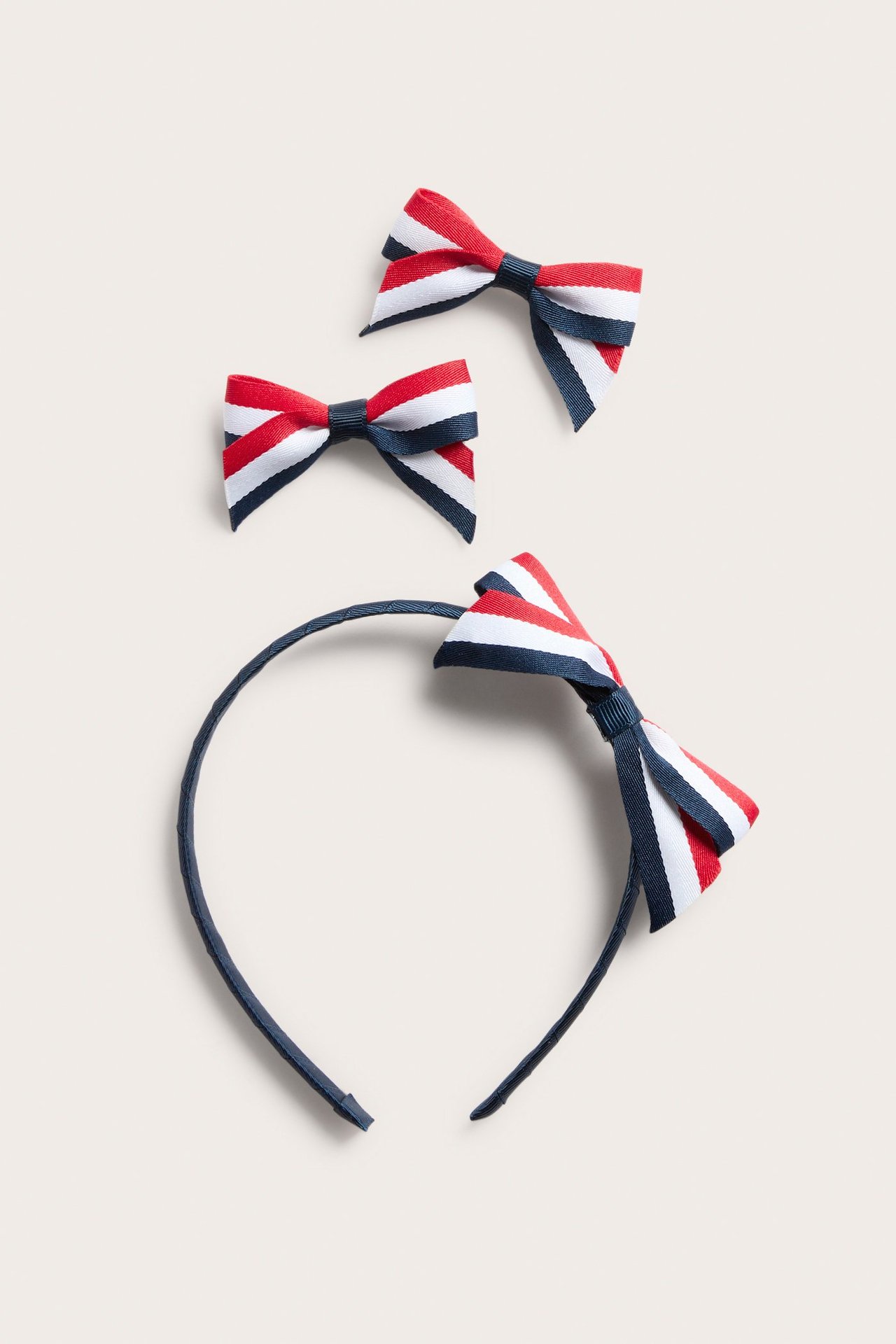 Widok z góry: granatowa opaska do włosów z kokardą w czerwono-biało-niebieskie paski i dwie pasujące spinki.