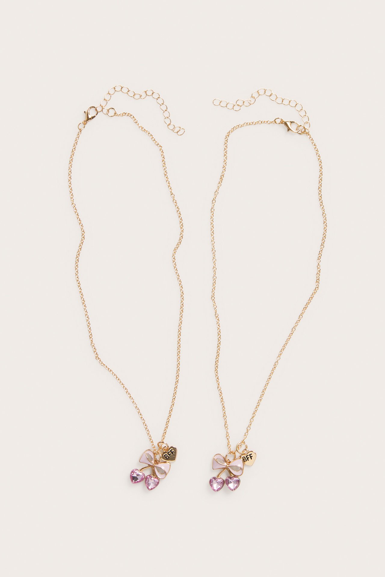 Toppvisning: to gullfargede BFF-halskjeder, hver med rosa sløyfe og to rosa hjerteanheng.