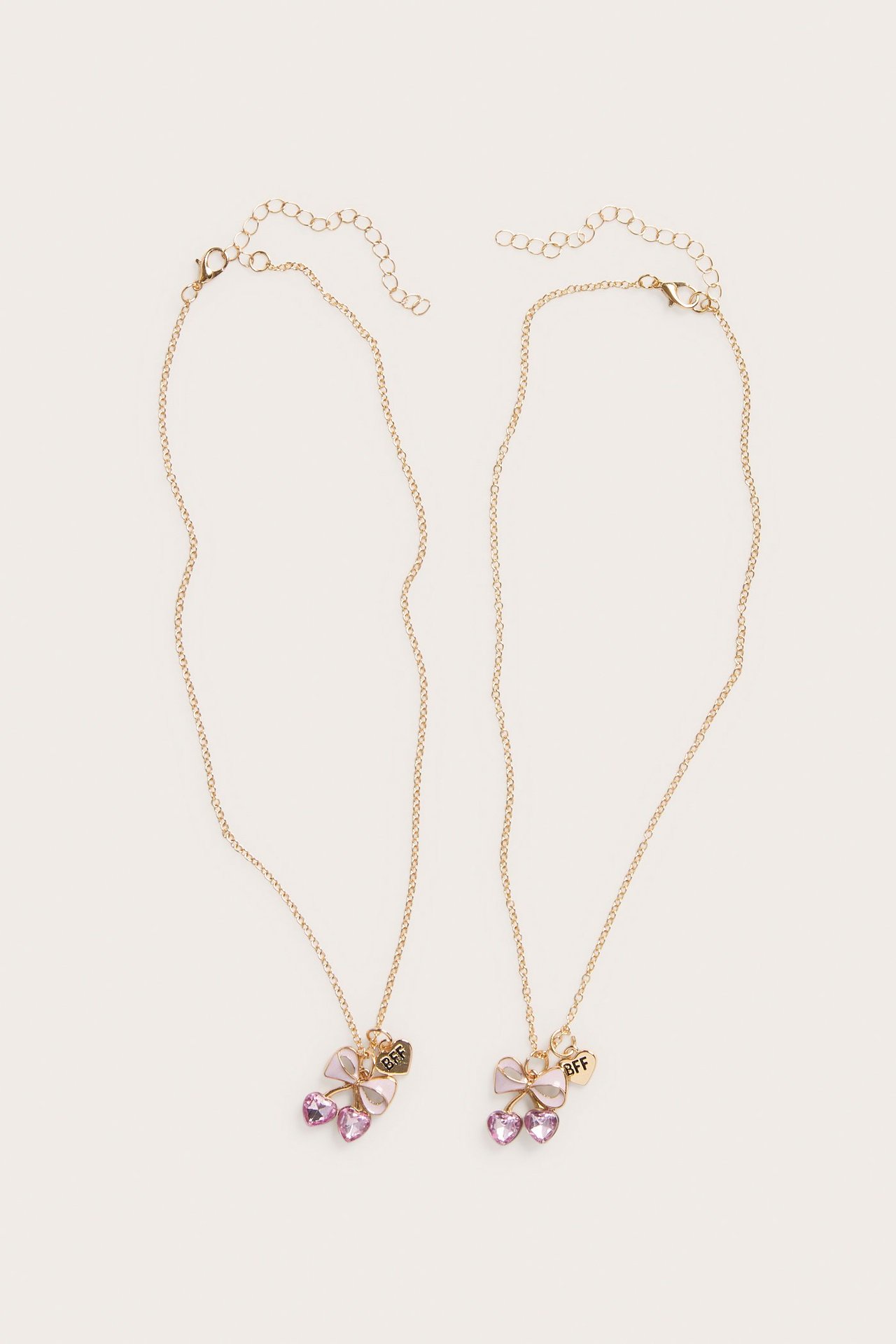 Widok z góry: dwa złote naszyjniki BFF, każdy z różową kokardą i dwoma różowymi serduszkami.