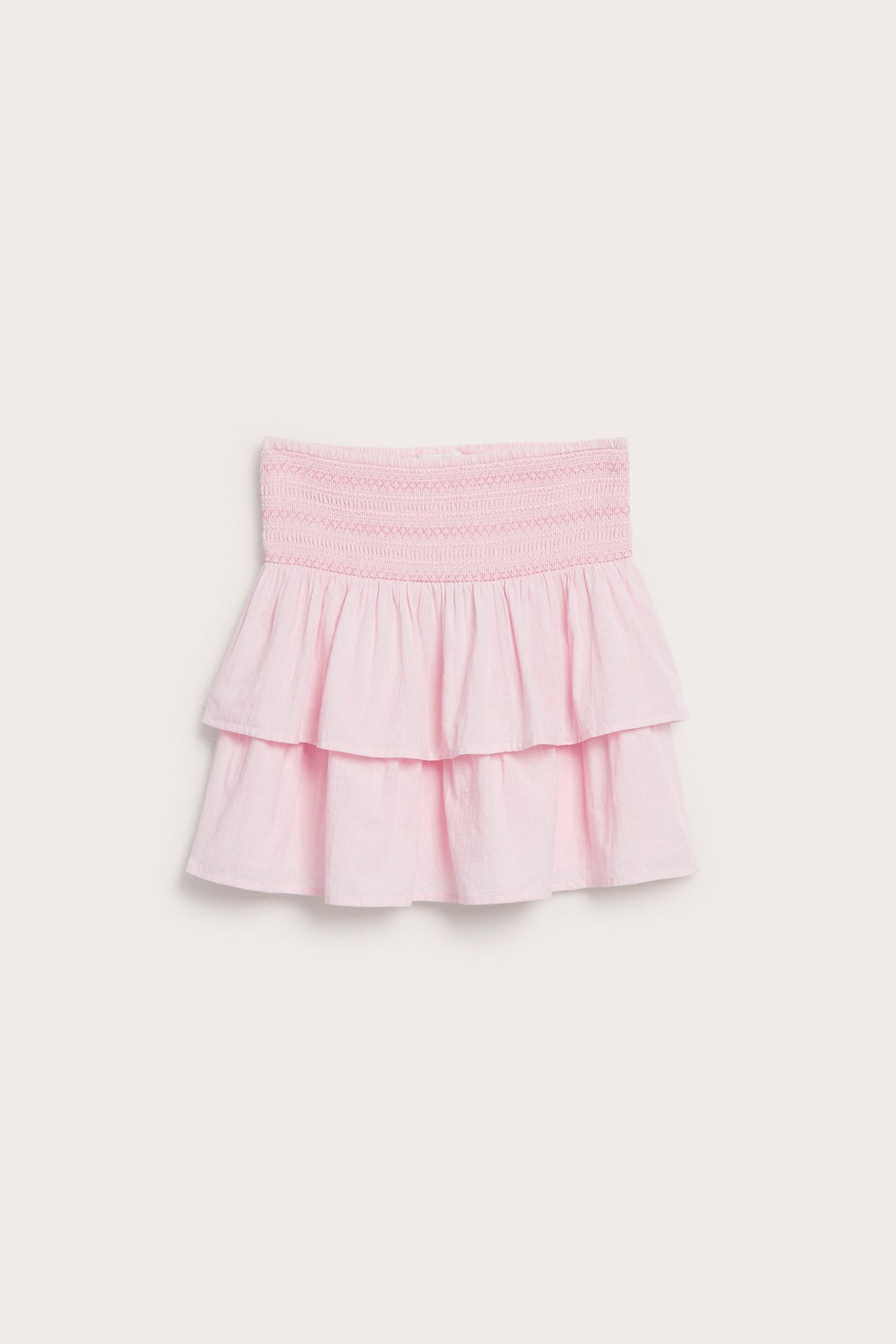 Edestä, lasten vaaleanpunainen yksivärinen, röyhelöhelmainen hame, jossa rypytetty vyötärö.