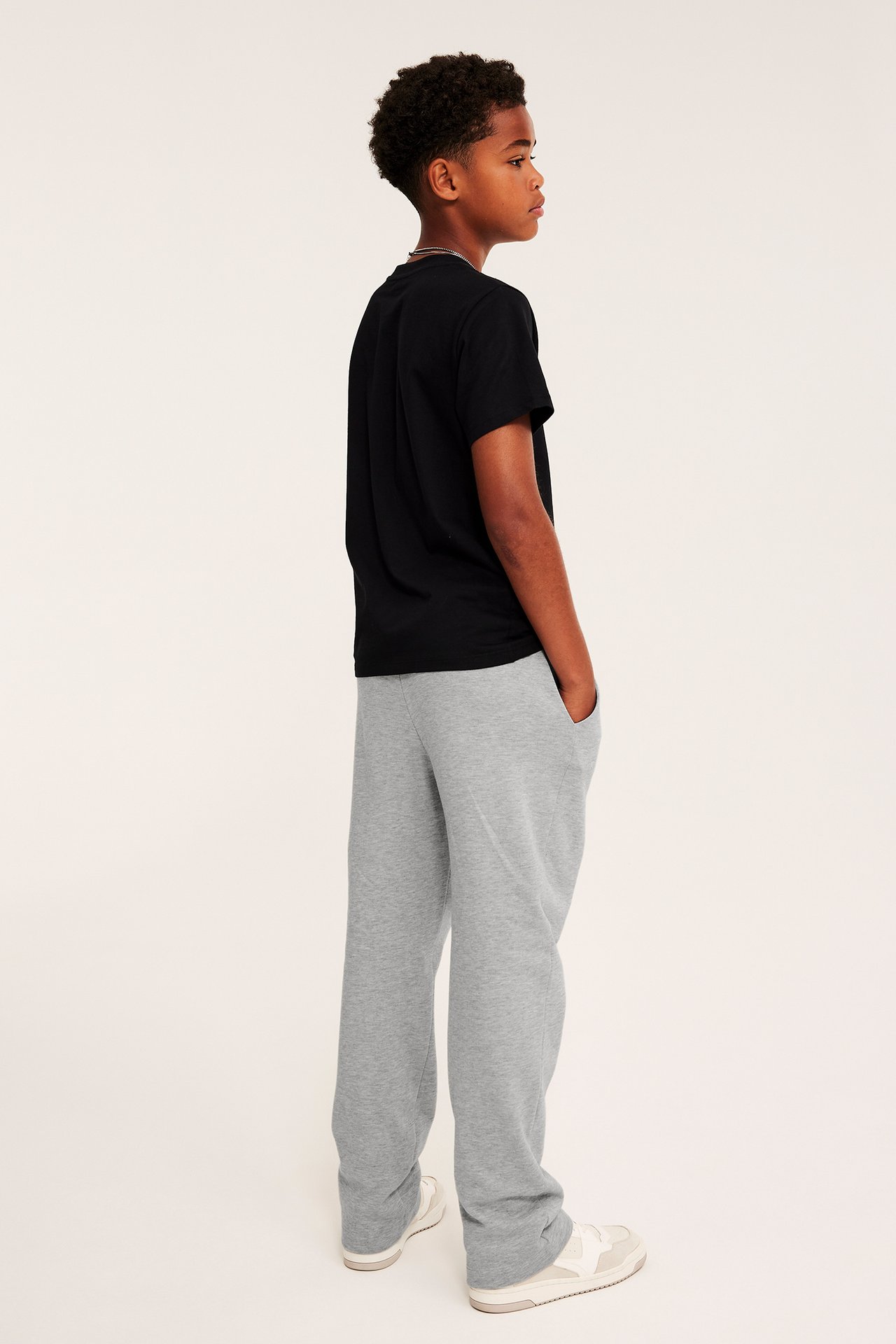 Sidebilde av et barn med gråmelert joggebukse, en svart t-skjorte og hvite sneakers.