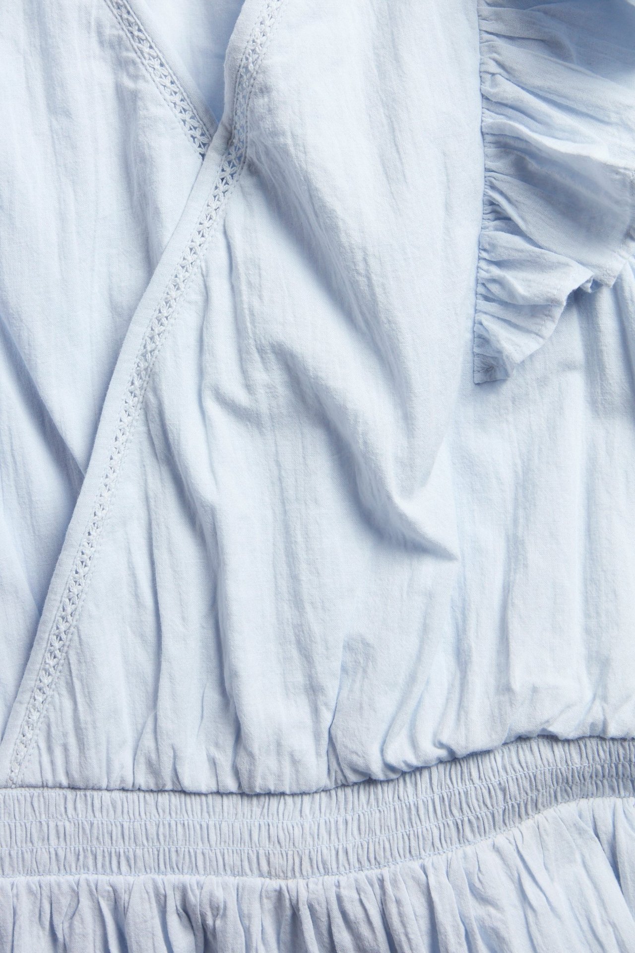 Zbliżenie jasnoniebieskiej bawełnianej sukienki z falbankami, koronką i marszczoną talią.