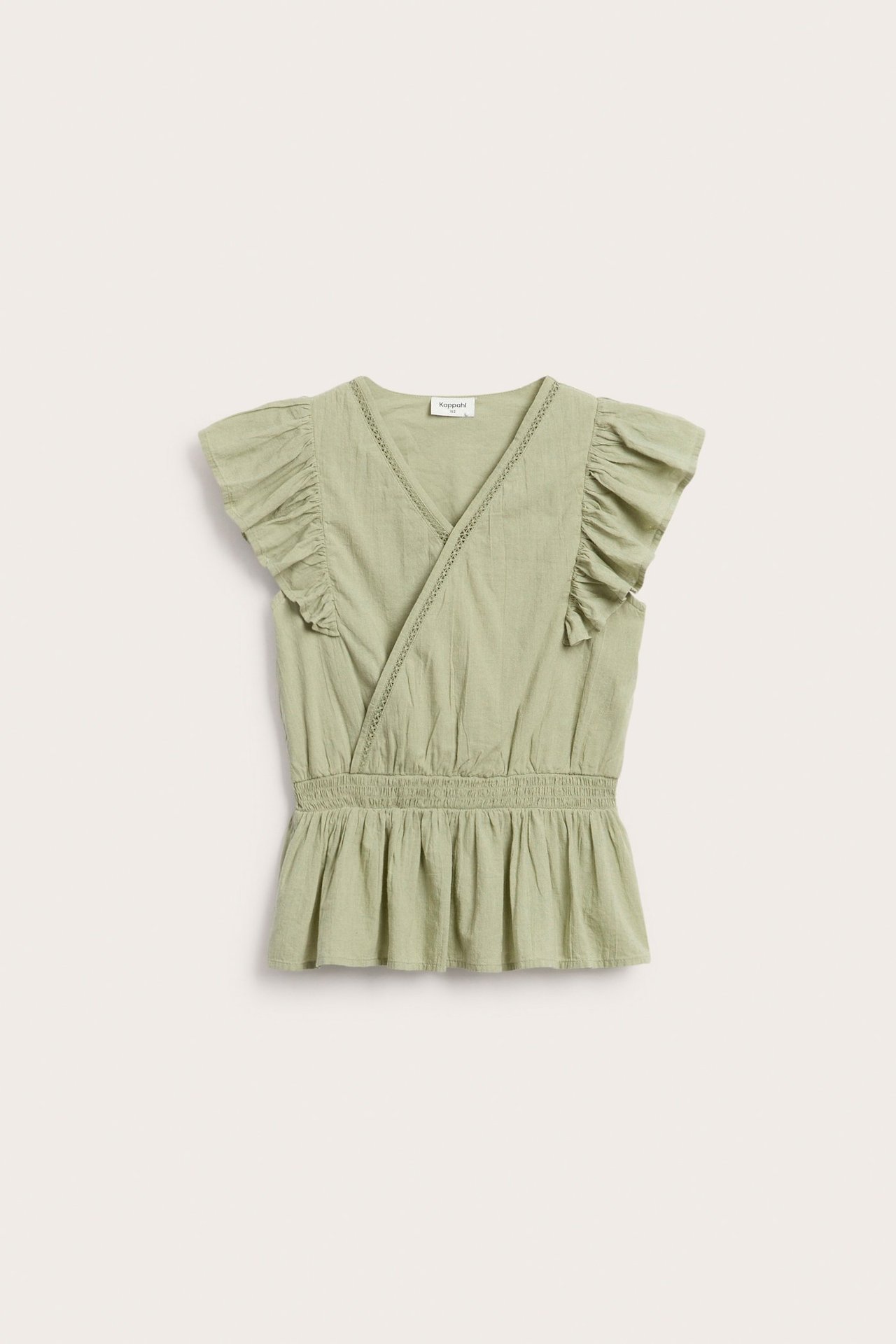 Frontvy av en grön volangblus i bomull för barn med spetsdetaljer och smockad midja.