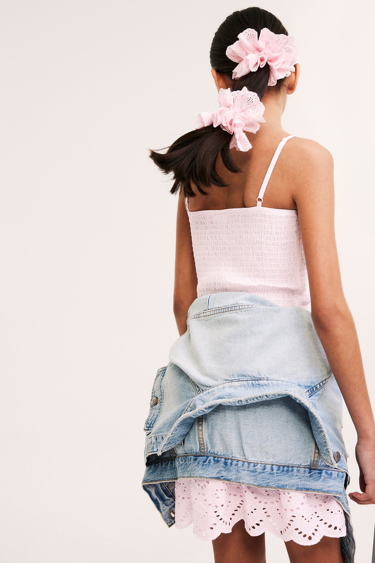 Barn, ryggvy: ljusrosa smockad bomullsklänning med broderie anglaise, ljusblå jeansjacka, två rosa scrunchies.