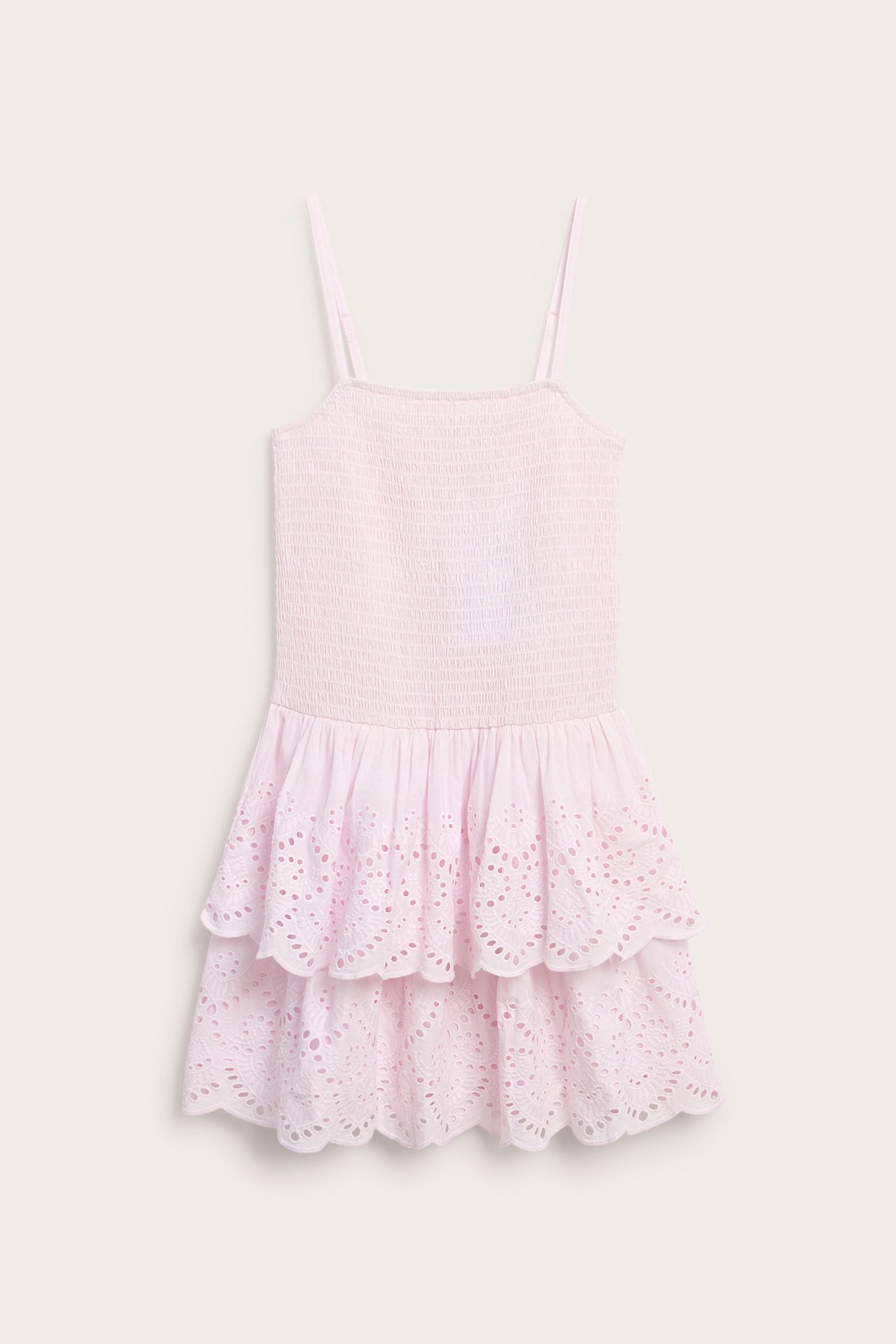Framifrån, en ljusrosa barnklänning i bomull med smockat liv och volanger med broderie anglaise.
