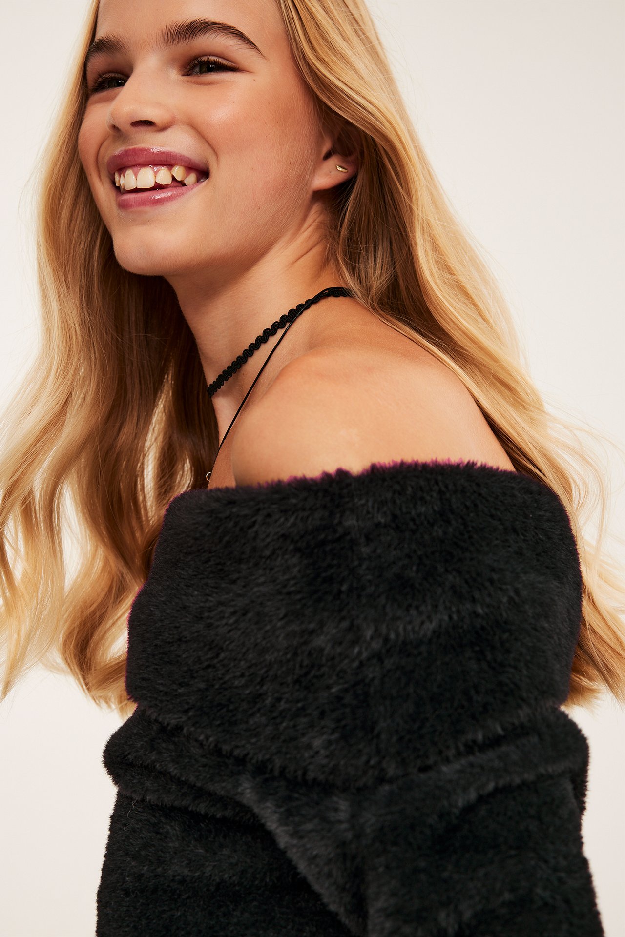 Nærbilde sideprofil av et barn i en svart lodden off-shoulder topp, svart choker og gulløredobb.